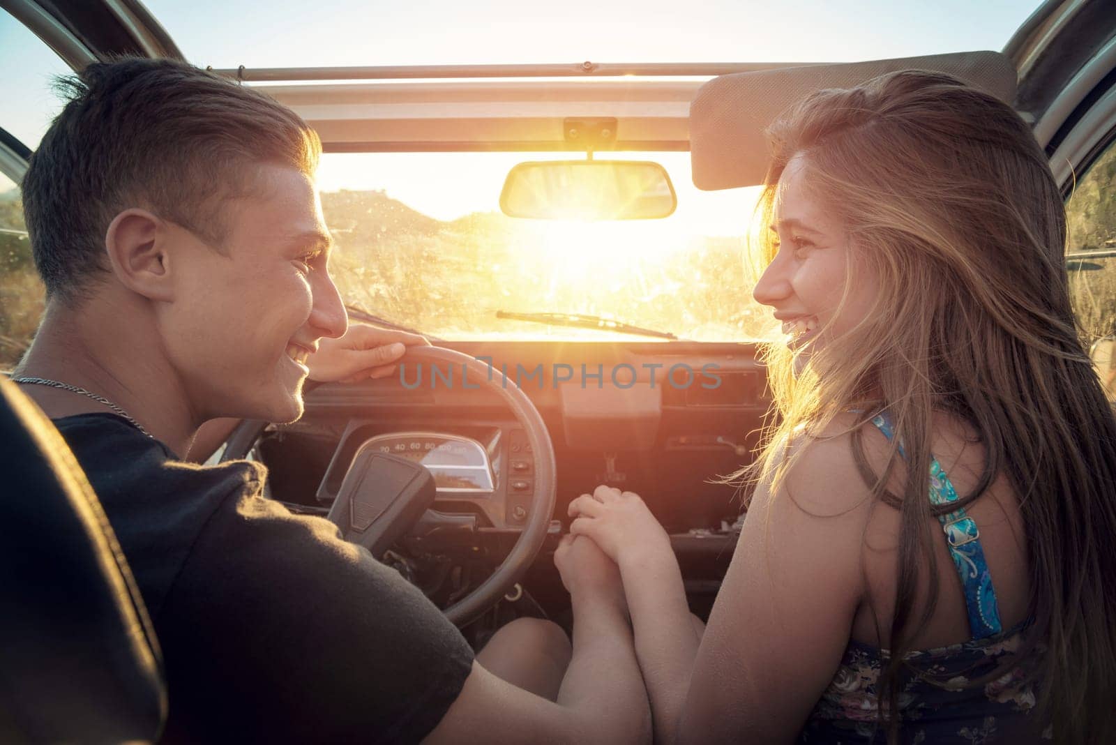 Happy young couple in a car enjoying the beautiful sunset in countryside.