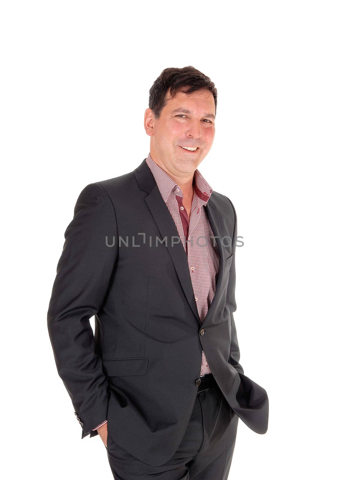 A happy businessman standing in a dark suit and checkered shirt with. his hands in in pocket, smiling, isolated for white background.