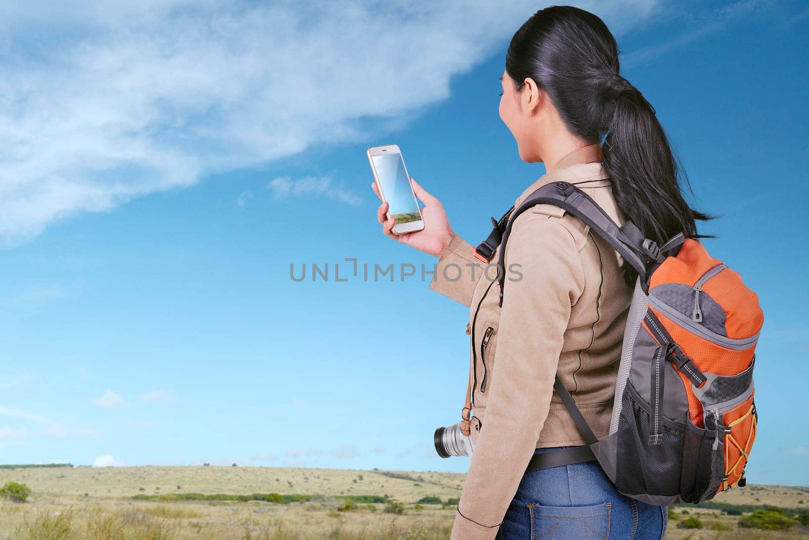 Young asian tourist woman looking at photos on her smart phone on the meadow