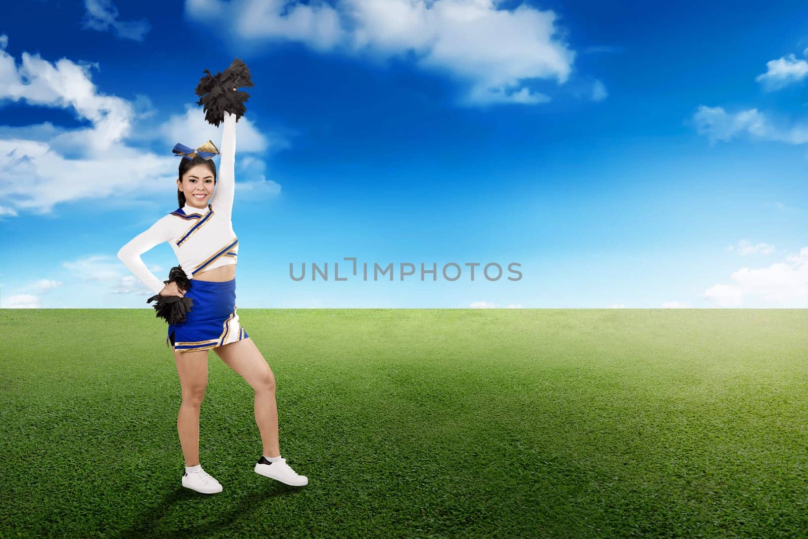 Happy asian cheerleader in action with pom poms on the field