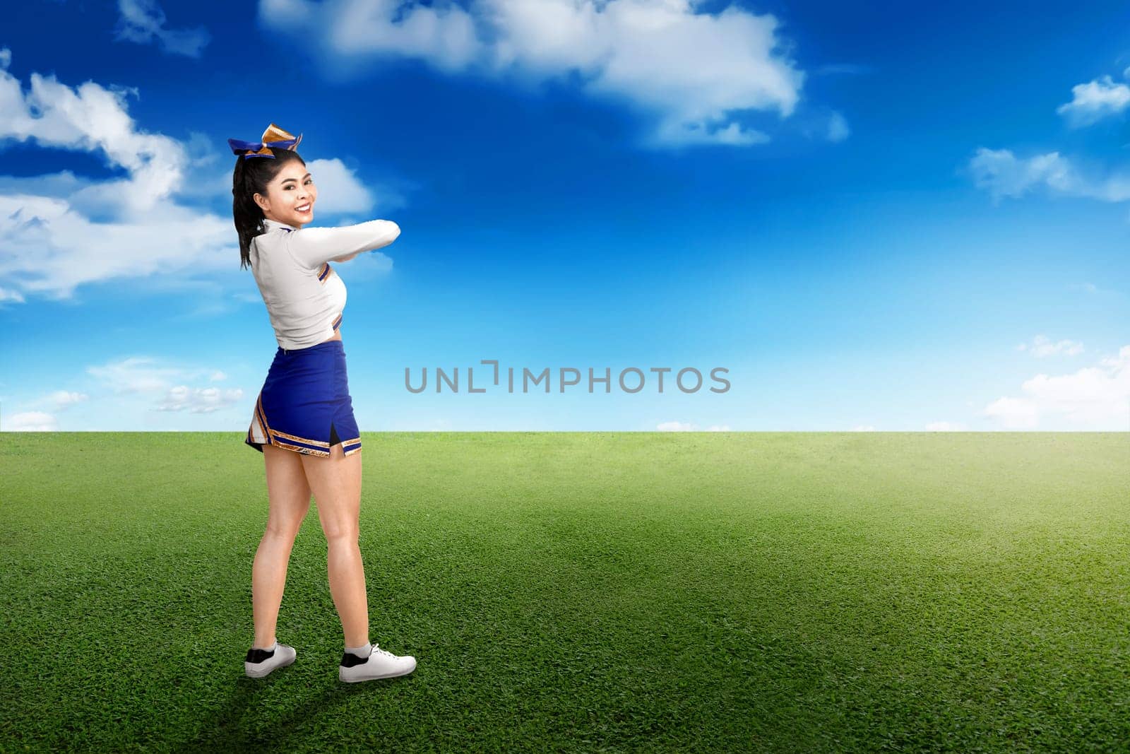 Back view of asian cheerleader in white and blue suit on green field