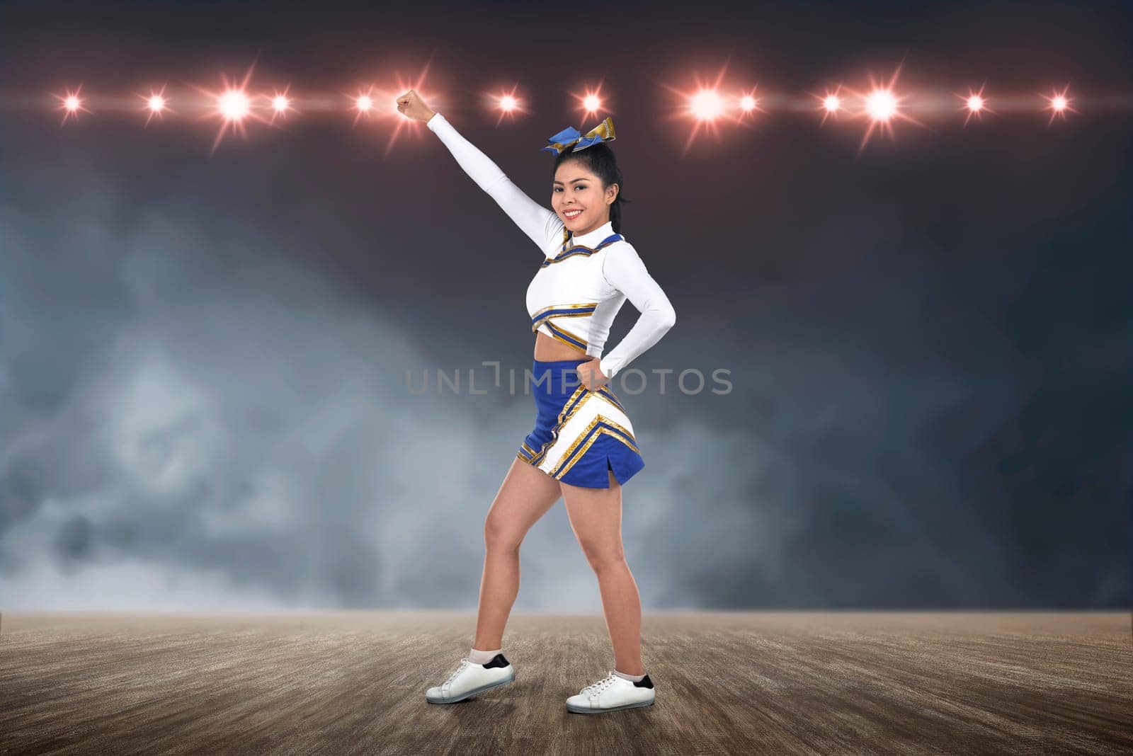 Attractive asian cheerleader in action with spotlights on background