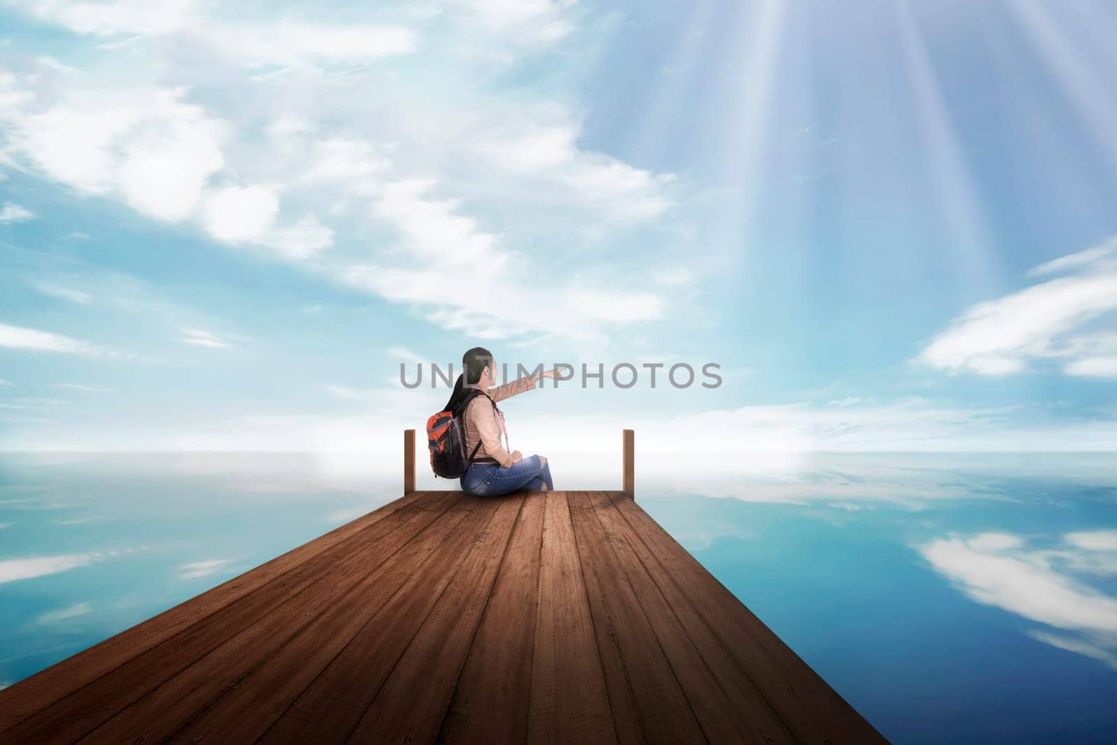 Young asian backpacker woman sitting and pointing blue sky at pier