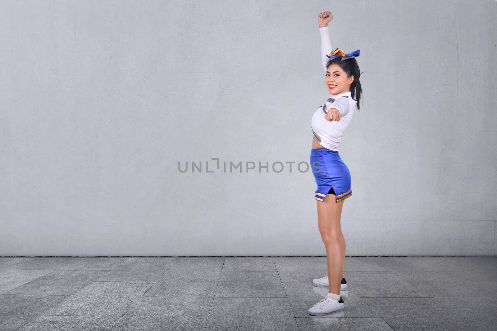 Smiling asian cheerleader in white and blue suit at indoor