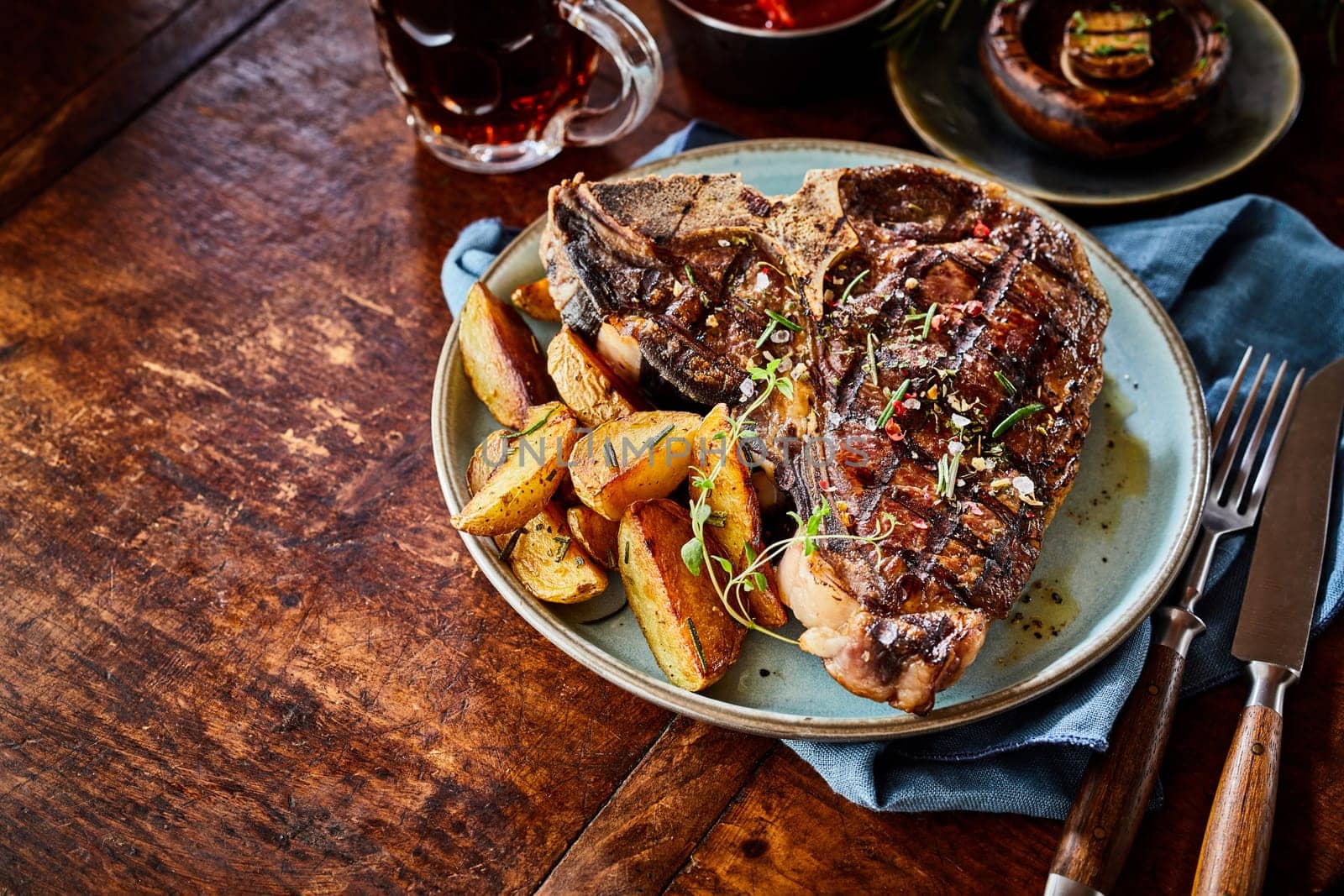 Grilled spicy T-bone steak with potato wedges served on an old rustic wooden table with copy space viewed high angle