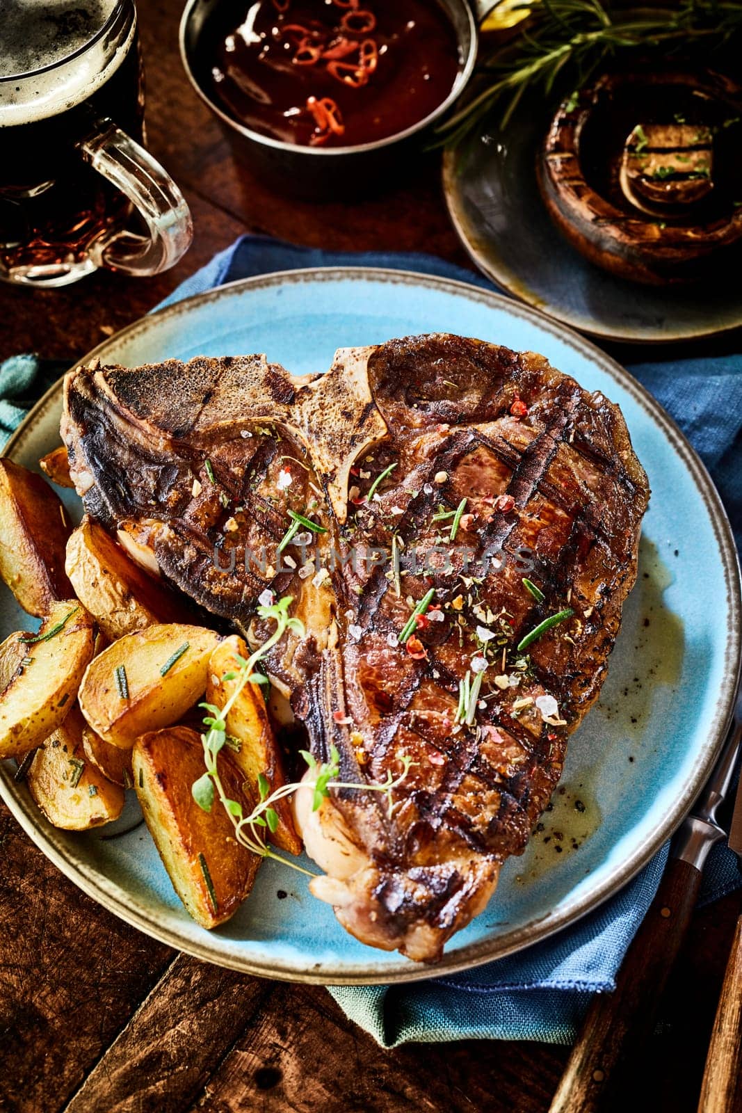 Barbecued T-bone steak with fresh herbs served with potato wedges , mushroom and a spicy sauce or dressing viewed high angle