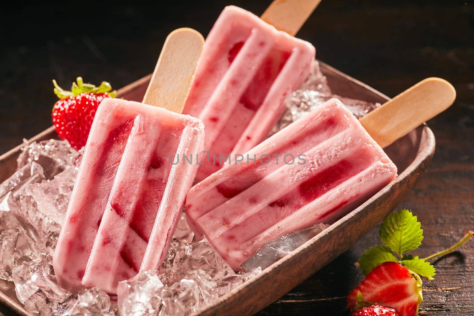 Three delicious summer snacks. Delicious frozen ice cream popsicle or ice lollies with strawberry and yoghurt on rustic plate.