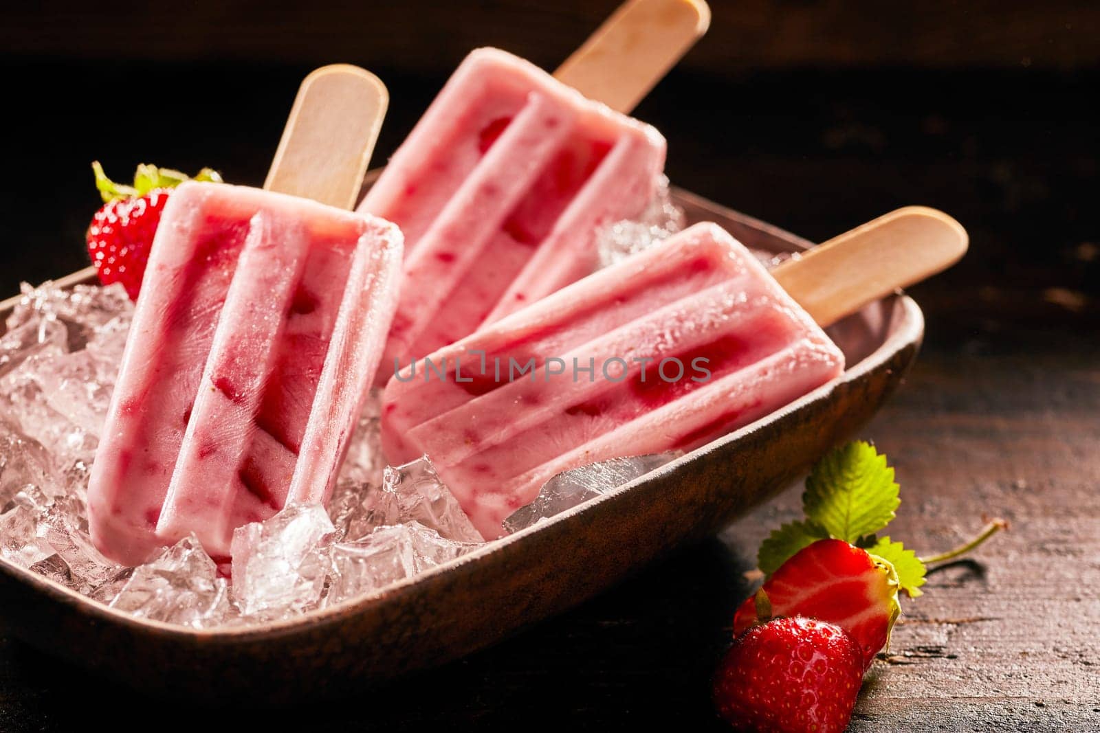 Tasty ice lolly with strawberries on a plate filled with crushed ice.