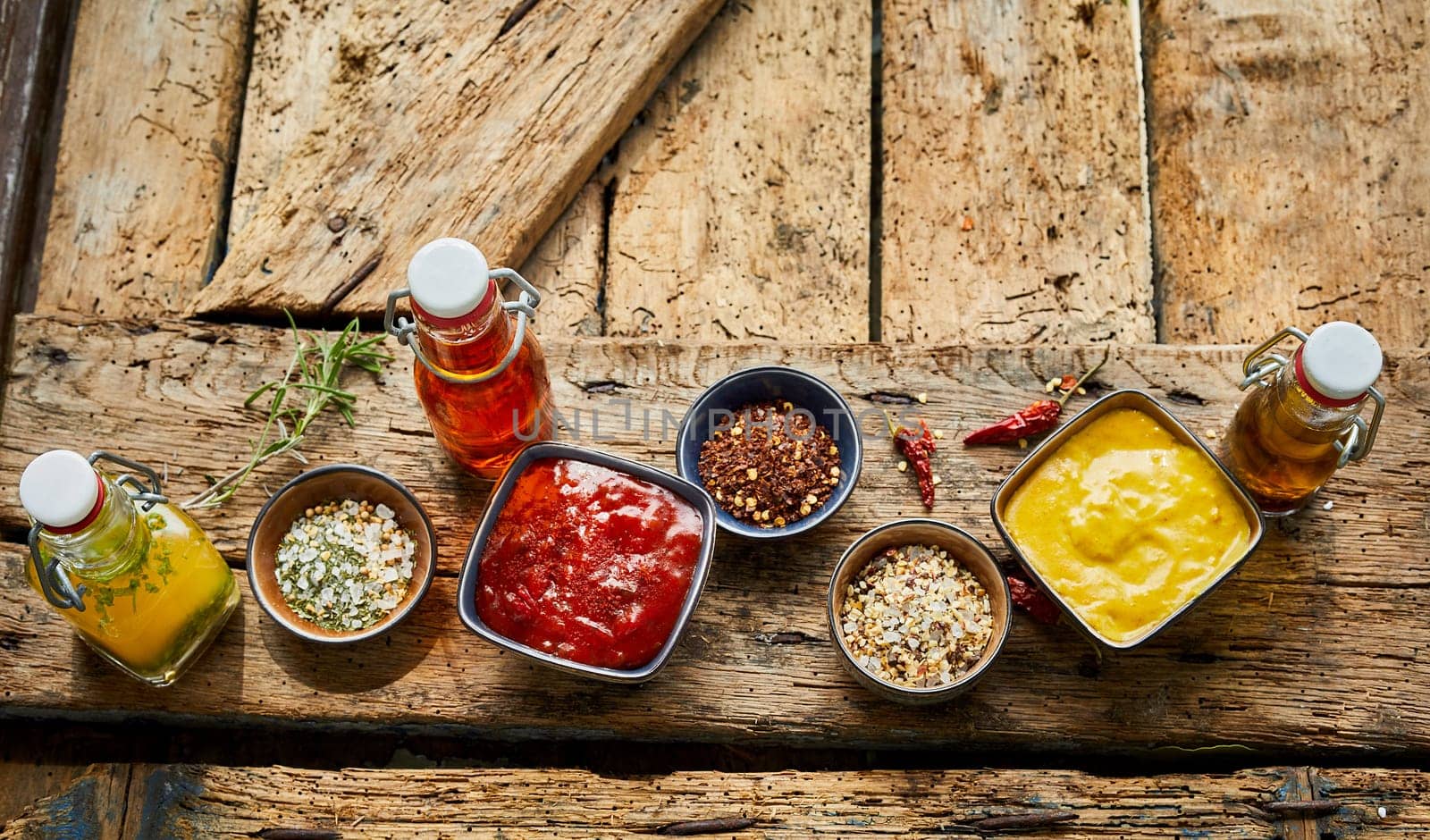 Spice rubs, ketchup, hot chili pepper, mustard and aromatic oils laid out ready for a summer BBQ or picnic on an old wooden rustic table with copy space viewed from above in panorama banner format