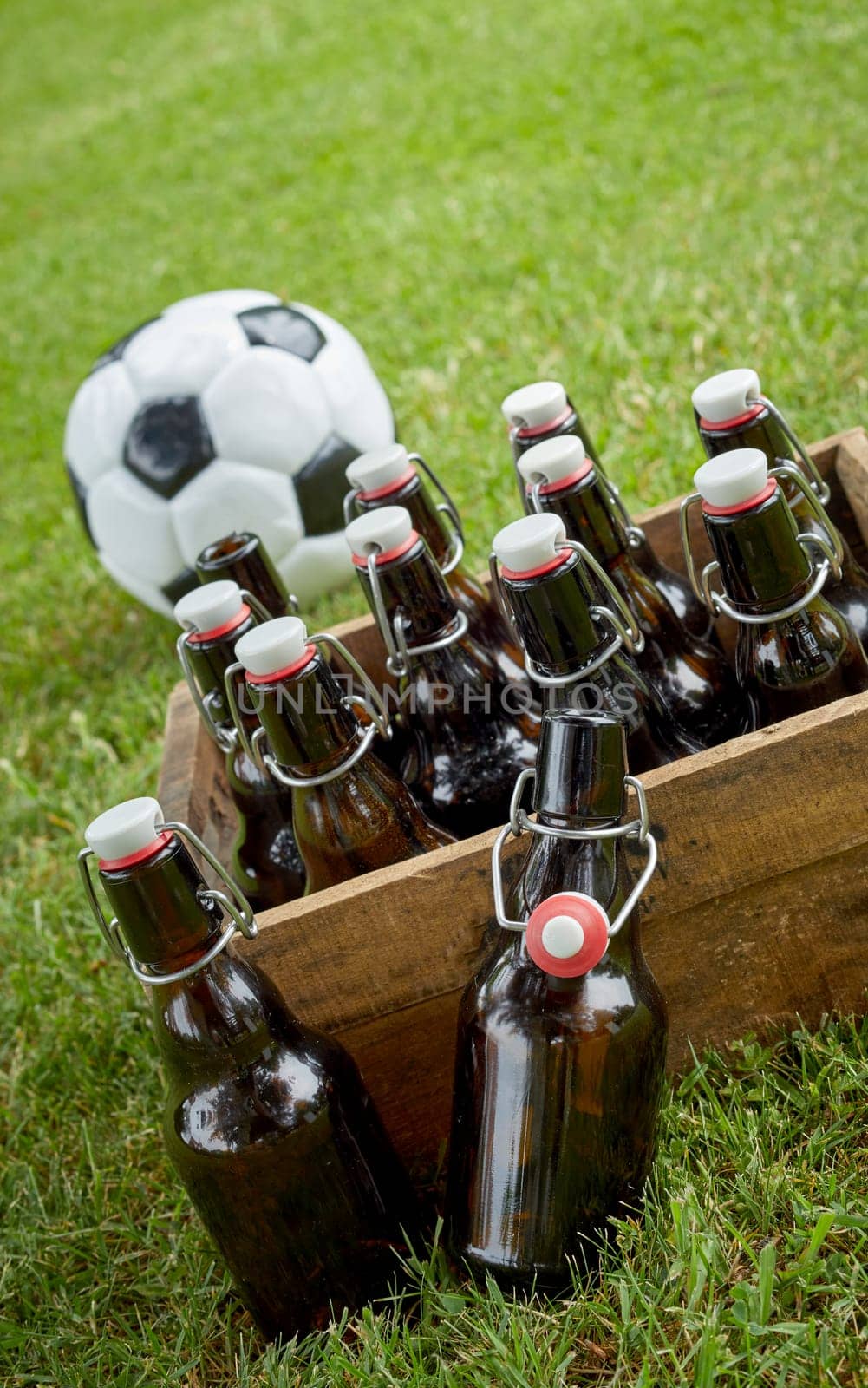 Bottled beer in an old wooden crate with a championship soccer ball on green grass ready for a party celebration and get together for the World Cup in a tilted angle close up view