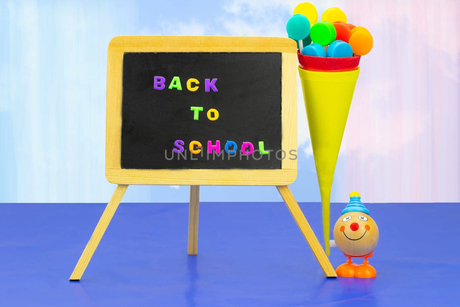 Colorful school equipment on dark blue table against light pastel colored background. Back to school written with colorful letters on blackboard. Space for your text or dsiplay product montage.