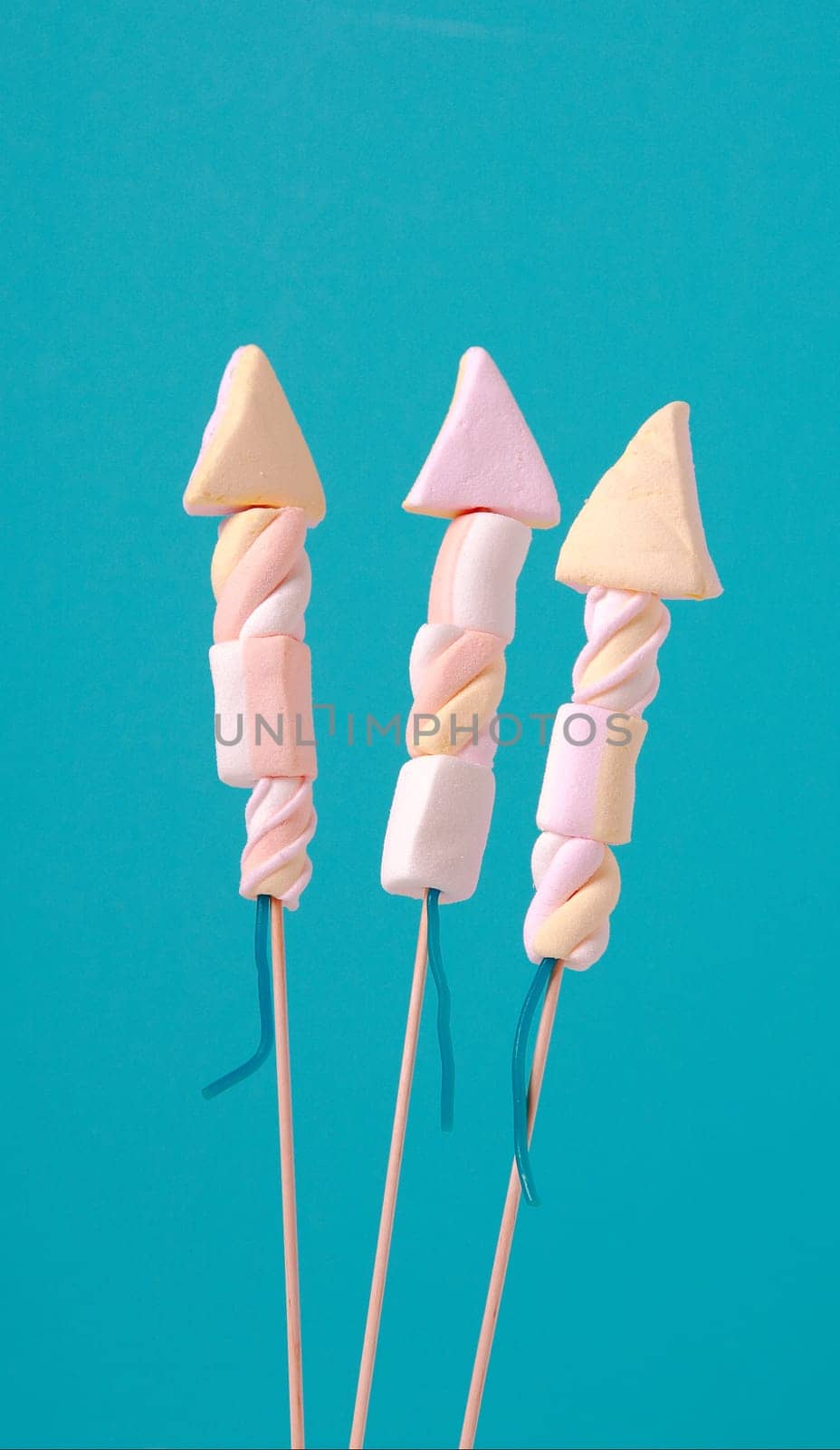 Three unique creative marshmallow edible fireworks in the shape of rockets for a party or holiday celebration on a turquoise blue background with copyspace