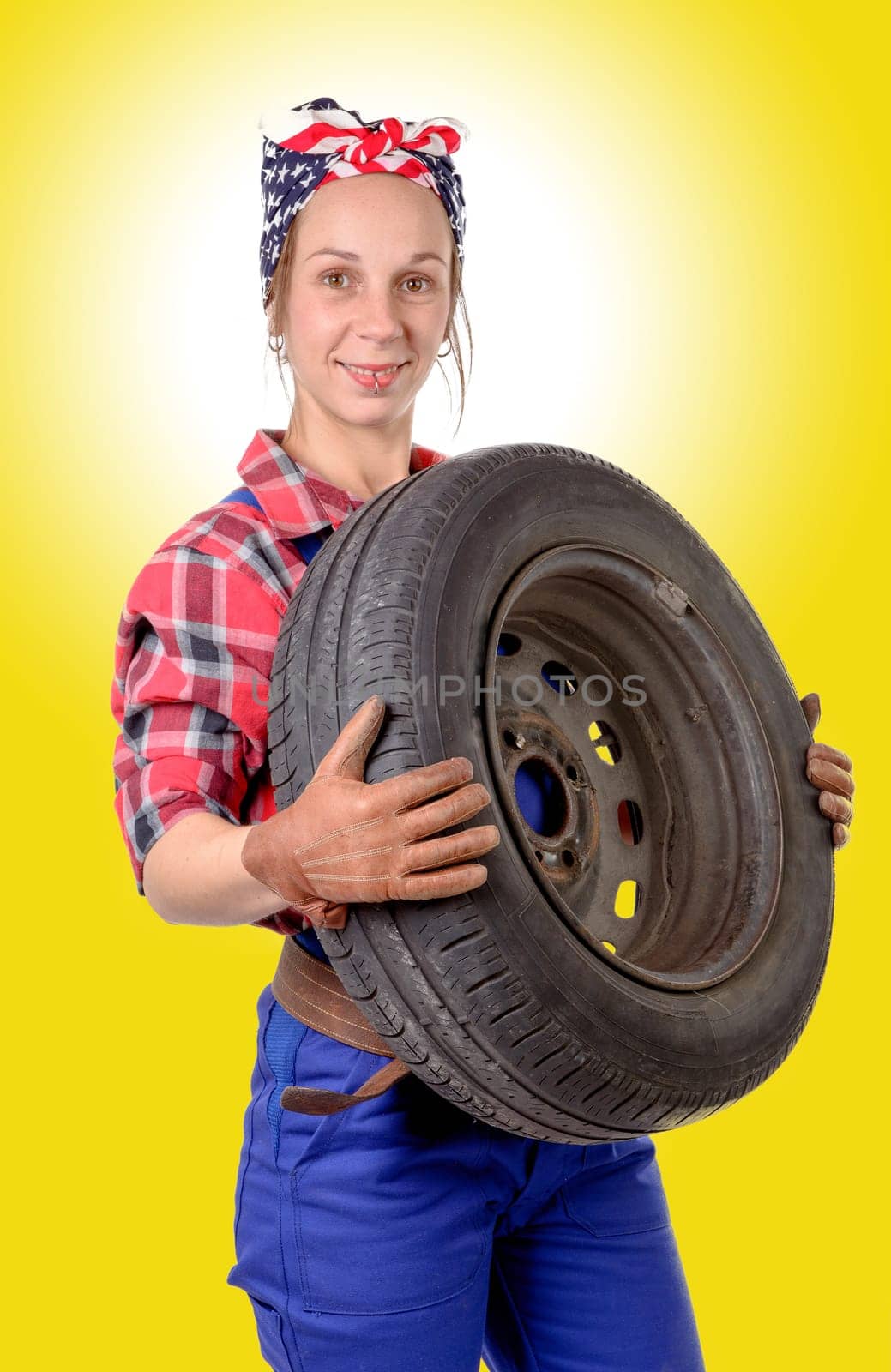 young woman mechanic with a car wheel on the yellow background
