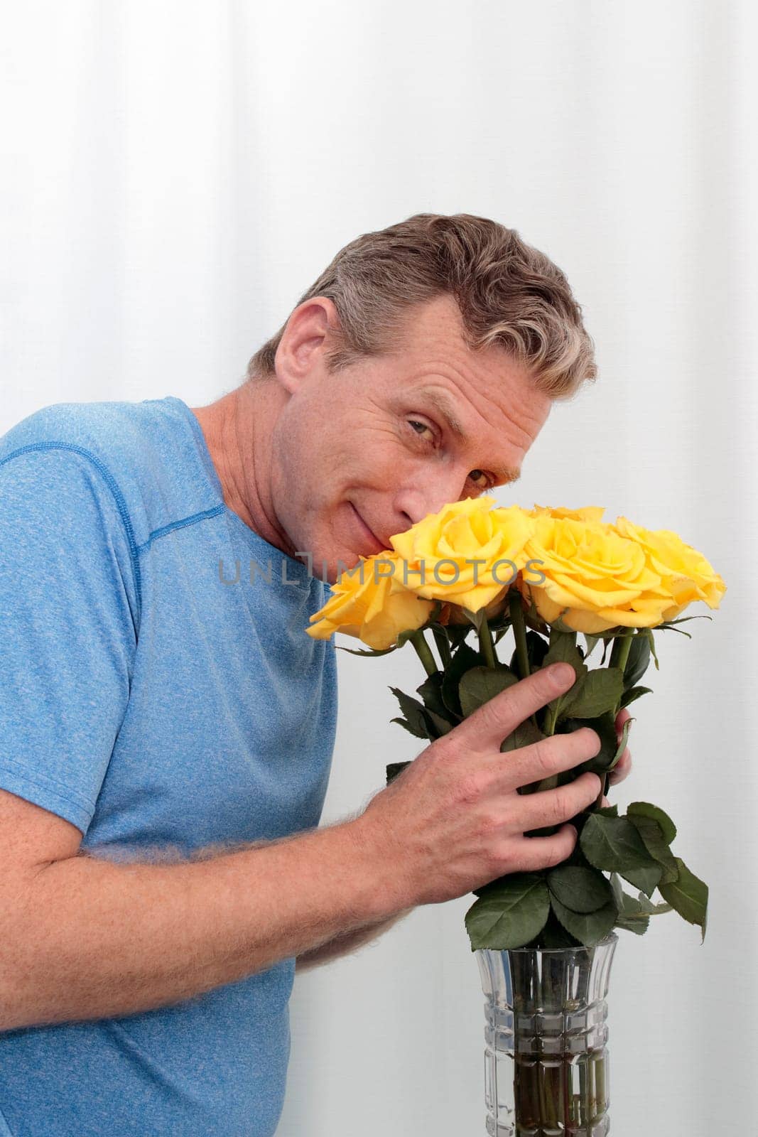 Mature male holds a dozen yellow pink roses happy. Man smilies smelling a bunch of aromatic roses. Middle-aged man holds a yellow pink roses bouquet, thankful for the aroma smiling at the viewer.