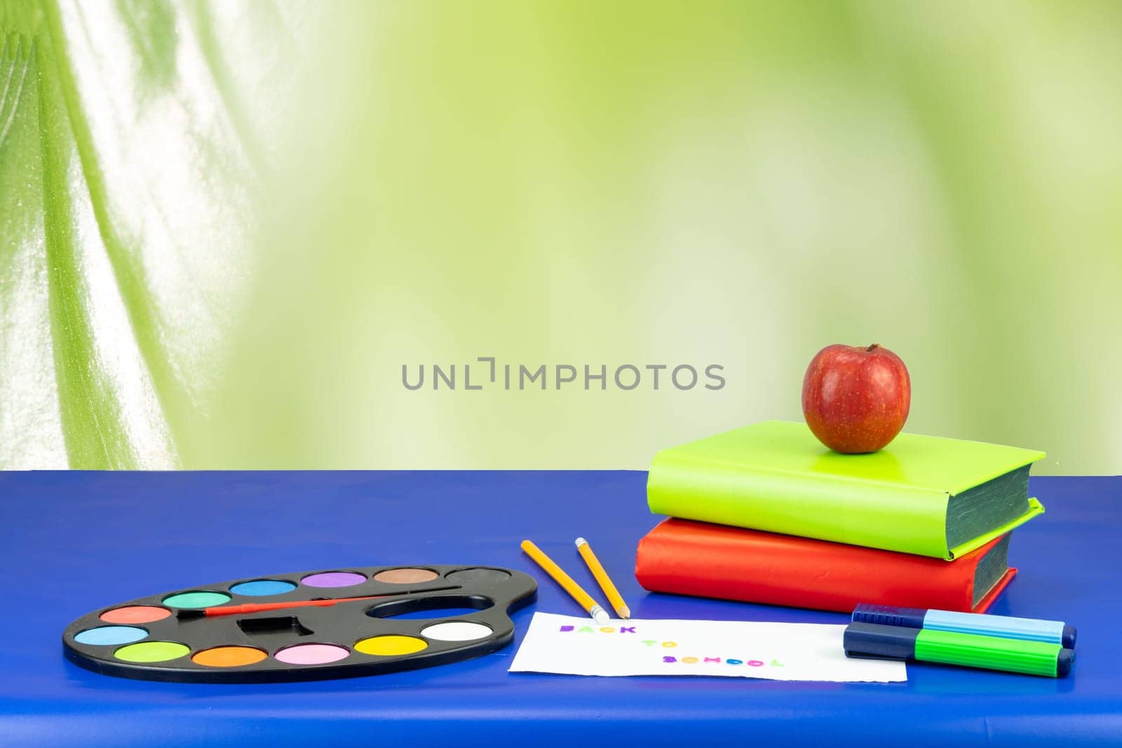 Colorful school equipment and two books on dark blue table against light green background. Space for your text or dsiplay product montage.