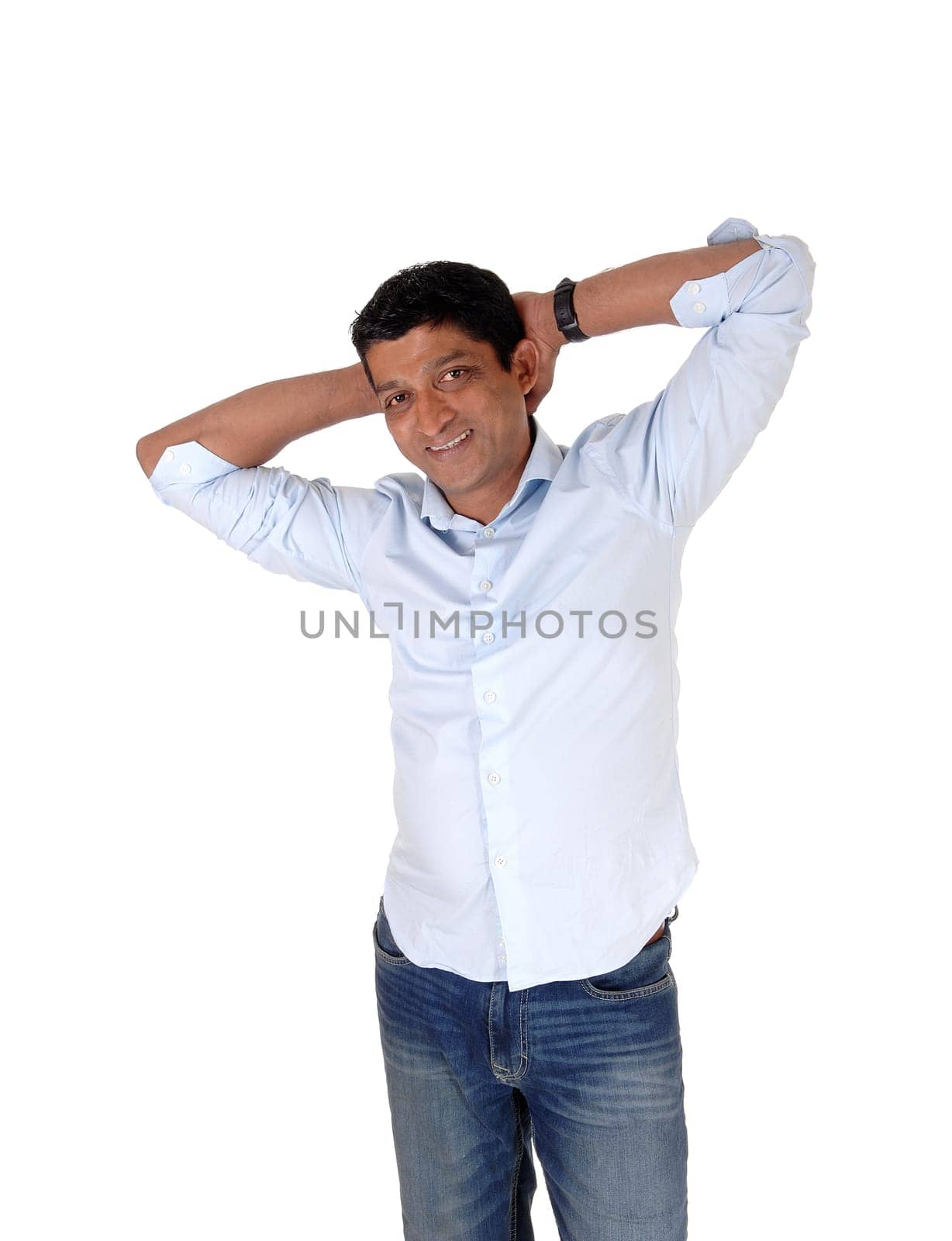 A happy smiling Asian man standing in jeans and a light blue shirt with.his hands behind his head, isolated for white background.