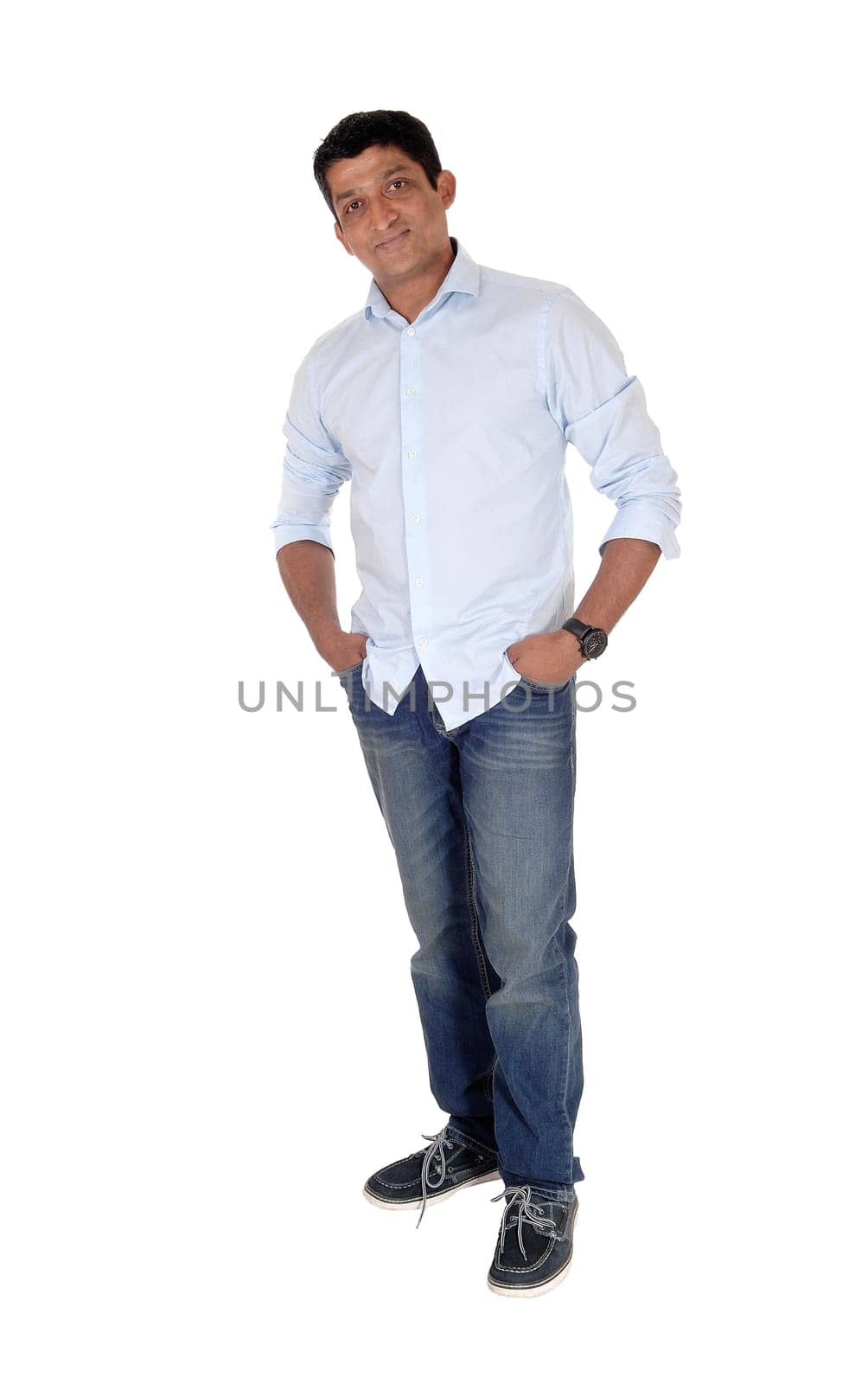 A tall East Indian man standing relaxed in jeans and blue shirt with.his hands in his pocket, isolated for white background.