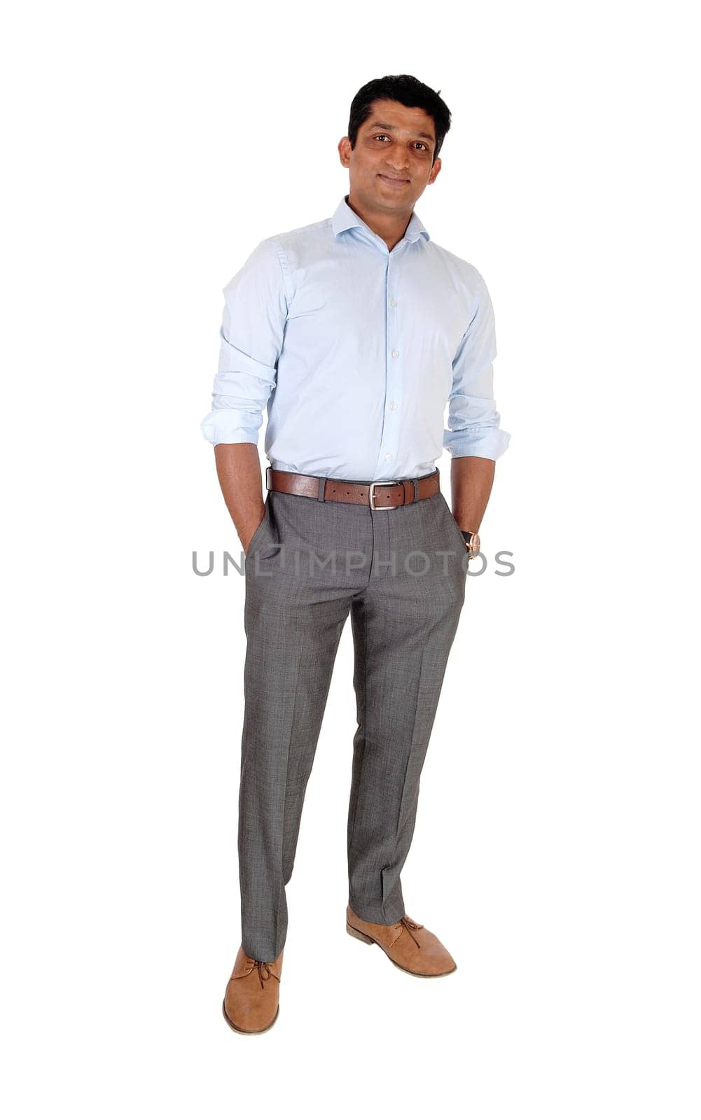 A tall East Indian man standing relaxed in dress pants and blue shirt .with his hands in his pocket, isolated for white background.
