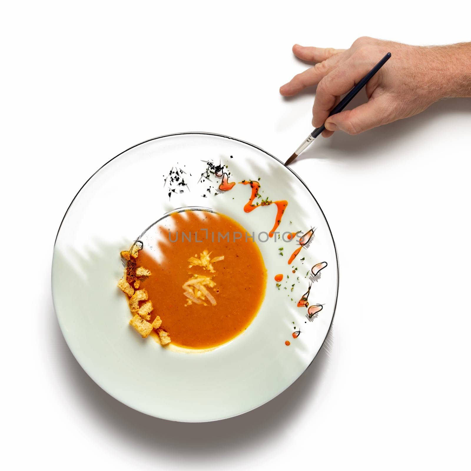 Hand painting over a plate of creamy vegetable soup. Concept for a cooking at the level of art.