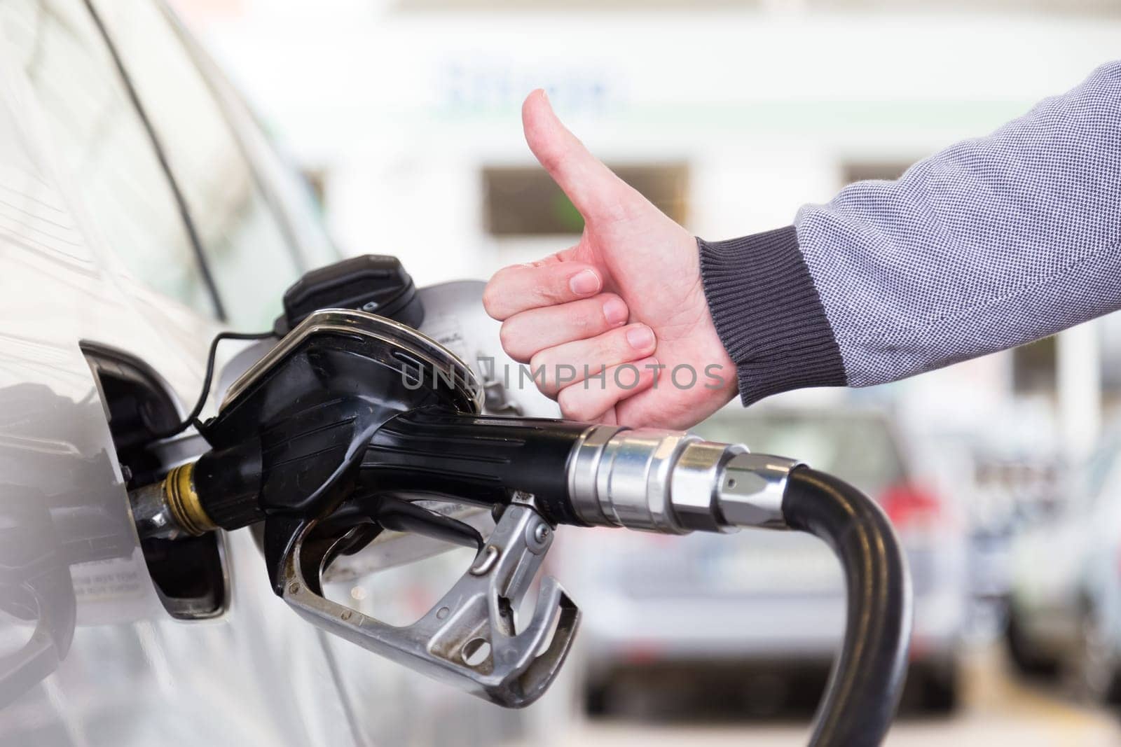 Petrol or gasoline being pumped into a motor vehicle car. Closeup of mans hand showing thumb up gesture, pumping gasoline fuel in car at gas station. Black and white image.