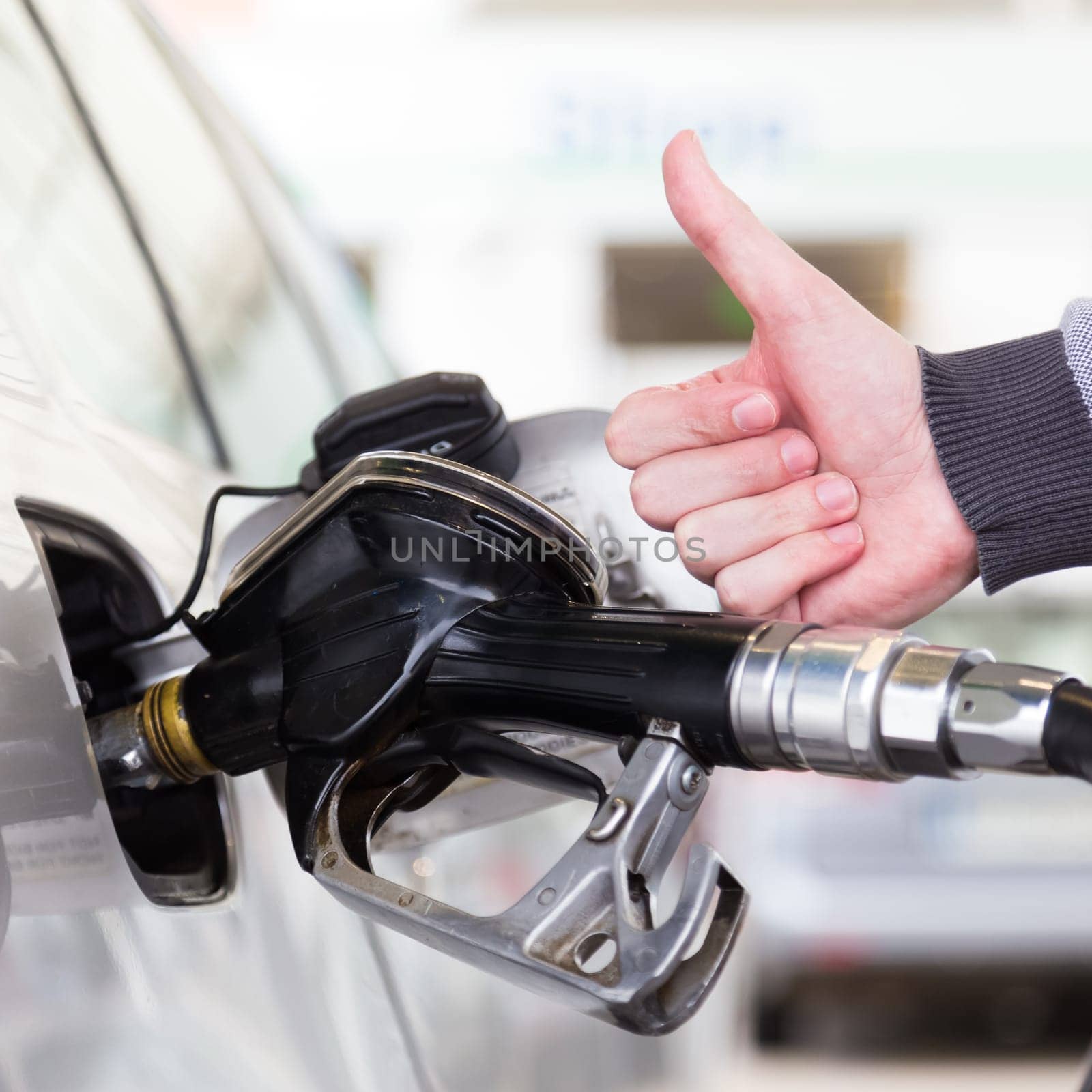 Petrol or gasoline being pumped into a motor vehicle car. Closeup of mans hand showing thumb up gesture, pumping gasoline fuel in car at gas station. Black and white image.