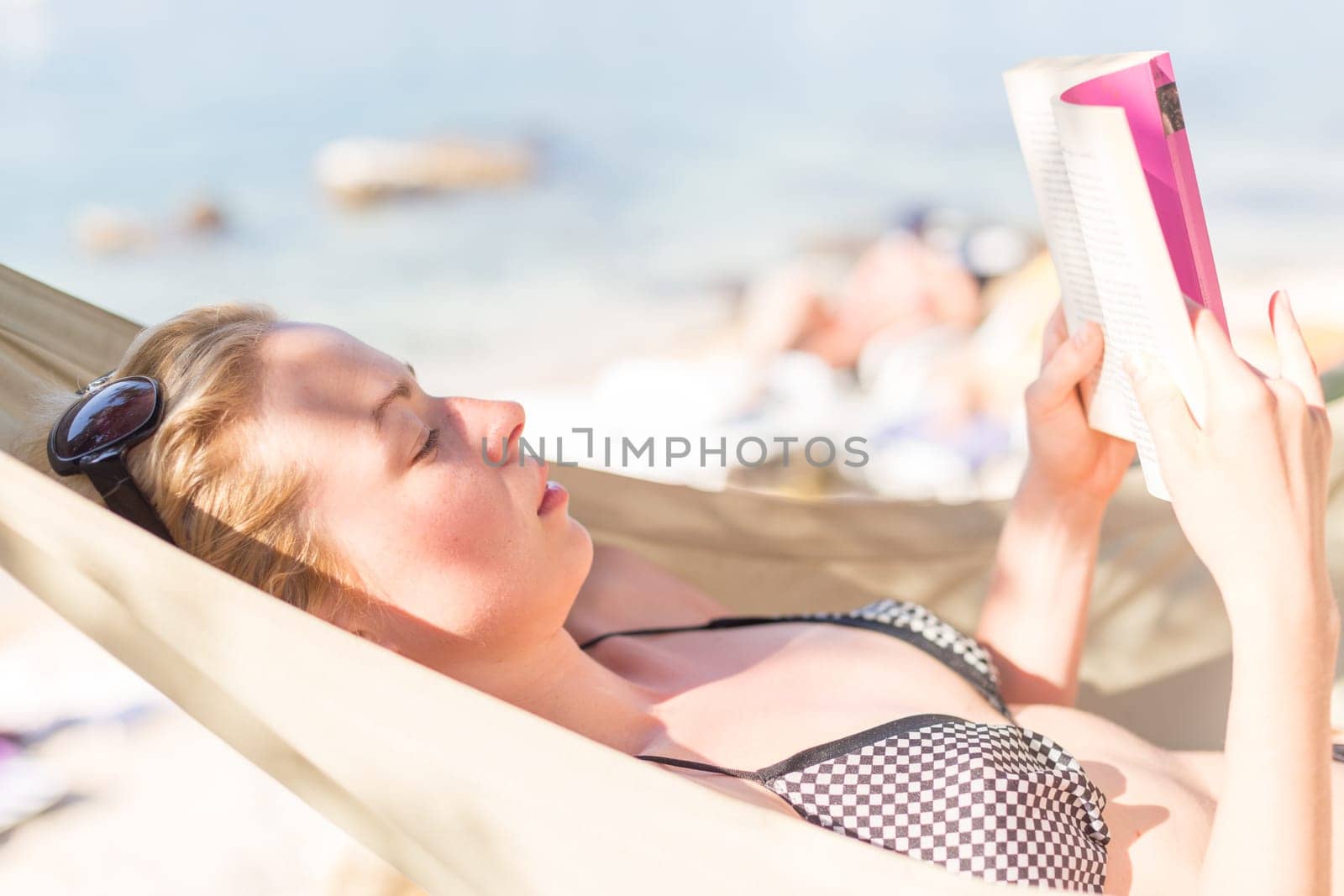Woman reading book in hammock on the beach. Summertime read.