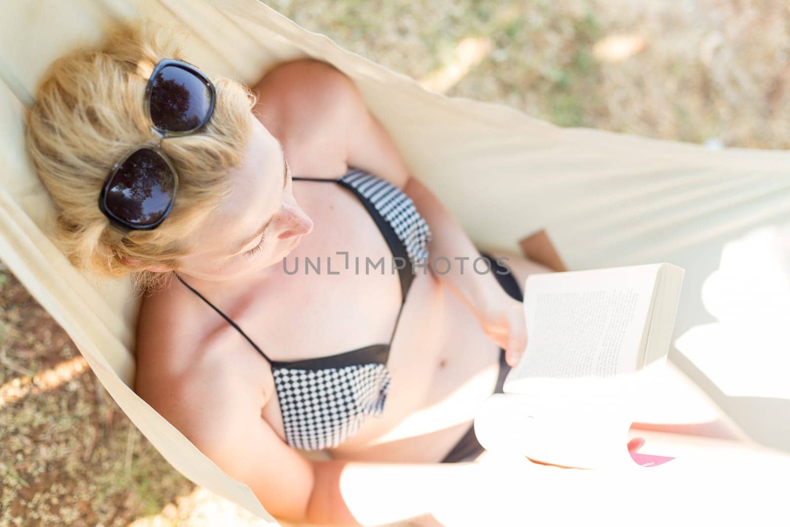 Woman reading book in hammock on the beach. Summertime read.