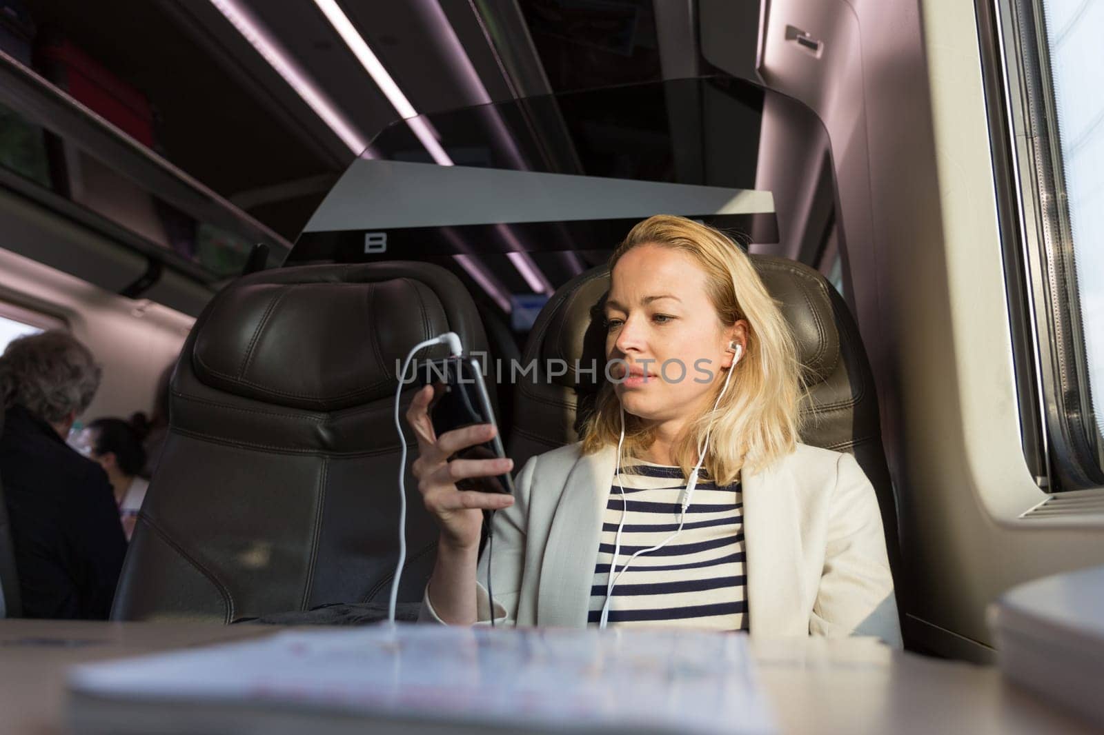 Businesswoman communicating on cellphone using headphone set while traveling by train in business class seat.