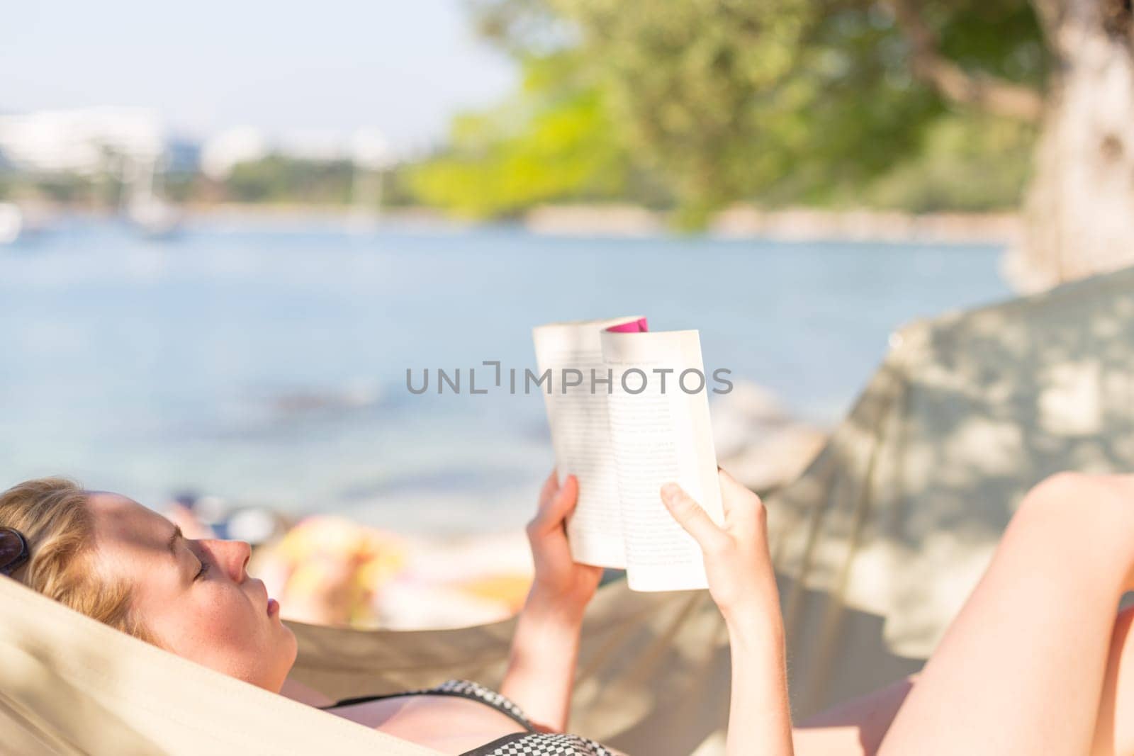 Woman reading book in hammock on the beach. Summertime read.