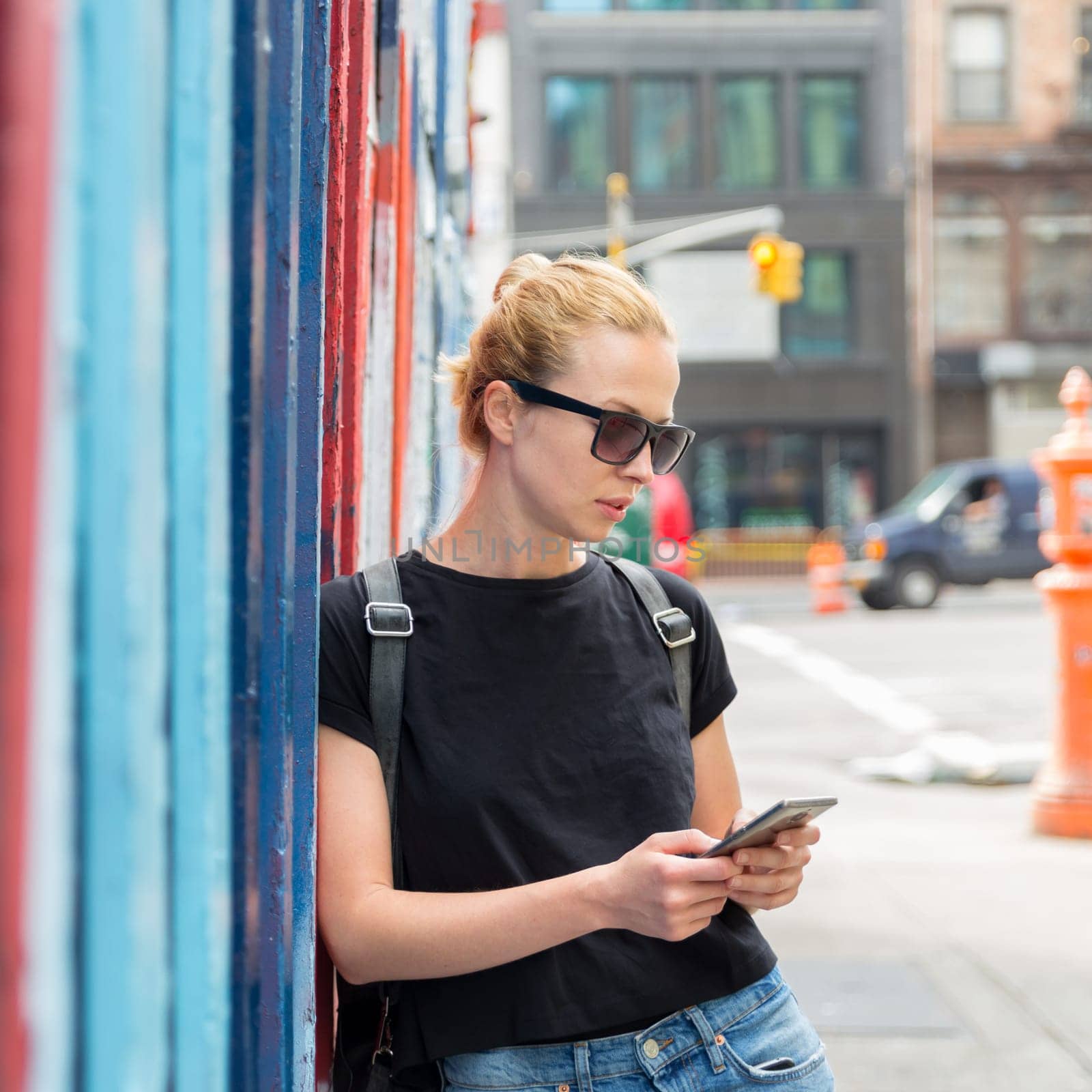 Closeup of female hipster with smart phone. Woman using smartphone against colorful graffiti wall in East Village, New York city, USA.