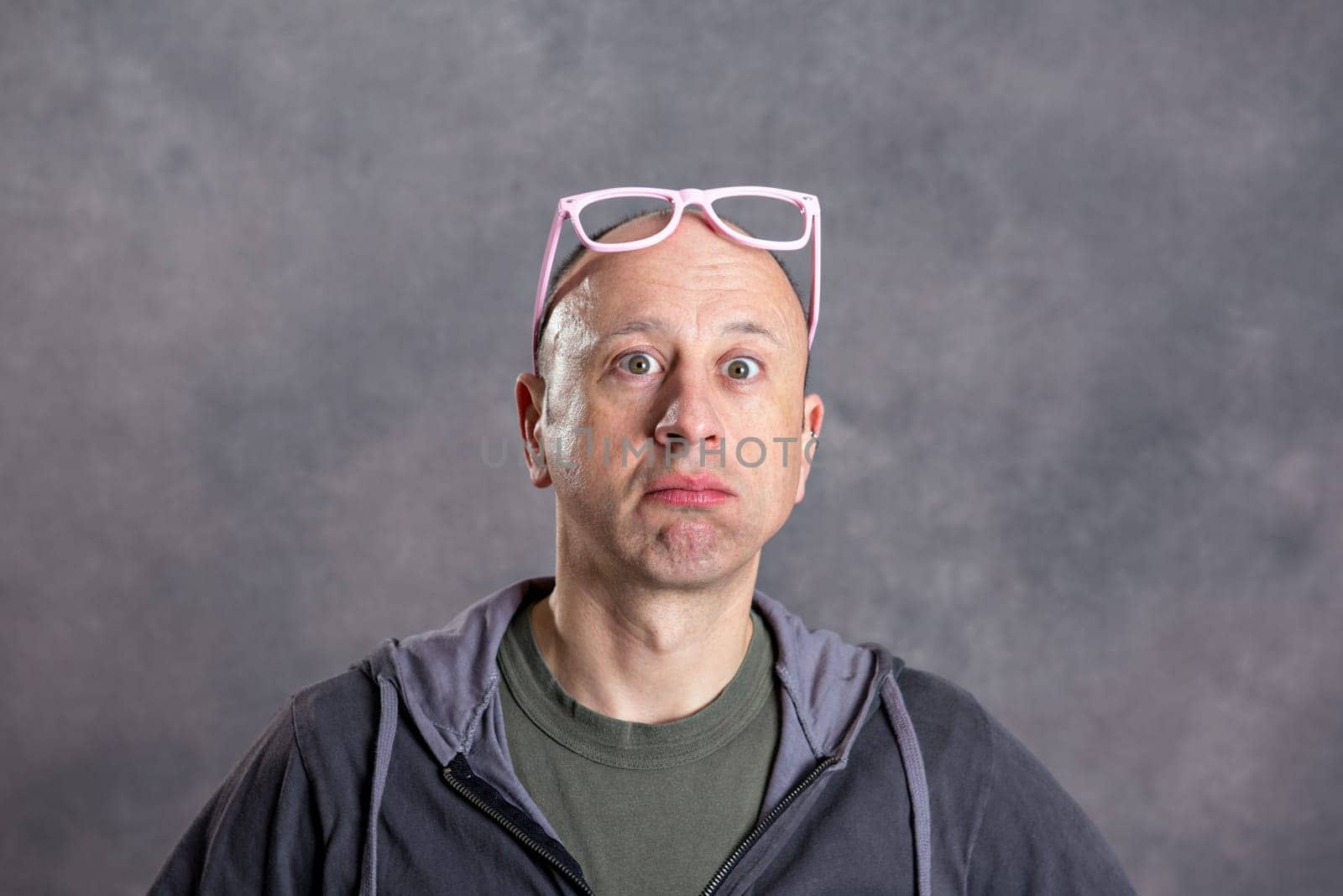 young man with pink glasses looking amazed in to the camera
