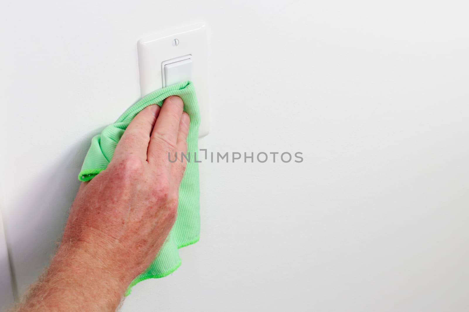 White panel light control cleaning by hand cloth. Male hand dusting light switch with cleaning cloth Flat white light switch control being dusted and cleaned with a green cloth by a caucasian male hand