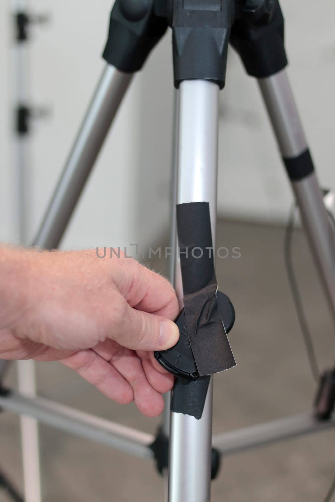 Fingers display camera remote control on tripodal. Hand holds camera remote control taped to a tripod Male hand showing camera remote control black gaff taped to a camera tripod in a tiled home office