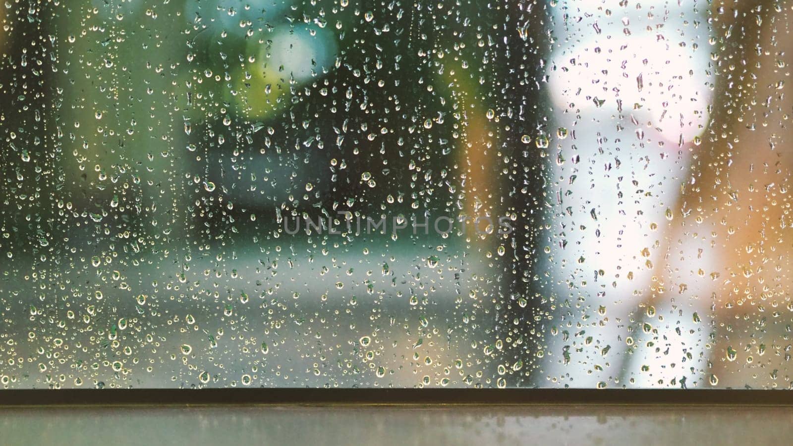Raindrops texture on the glass window frame of cafe room and nature background in rainy season