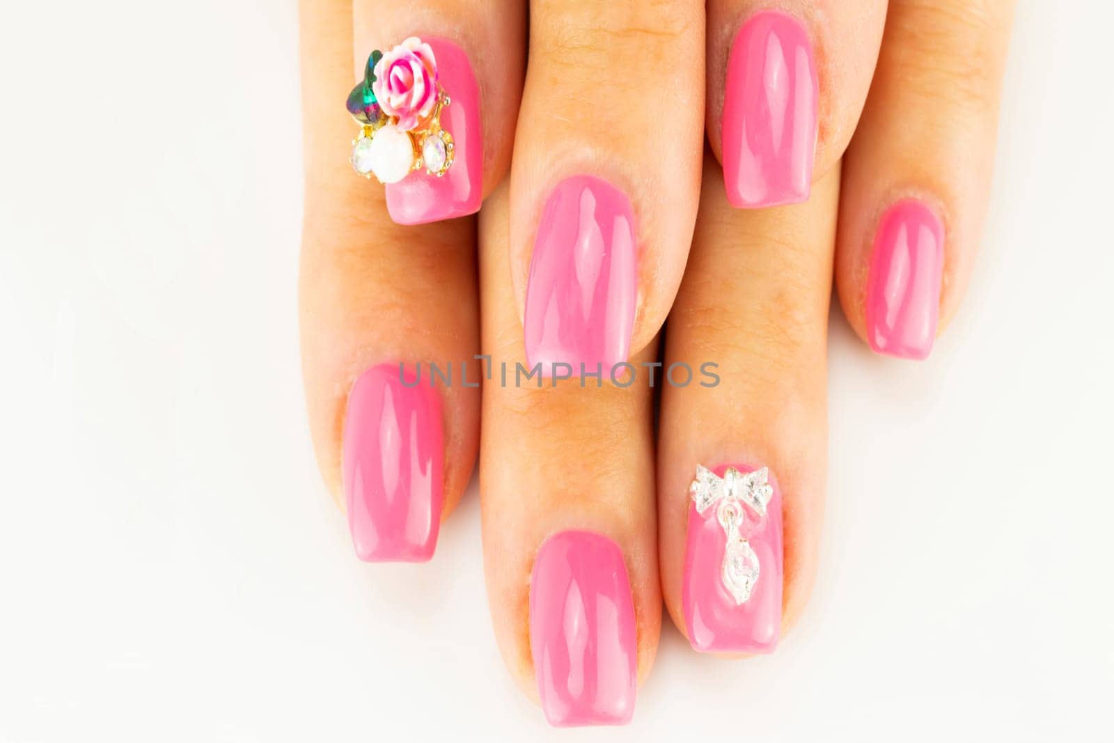 Closeup of beautiful pink nail design at female fingers on white background. Two figure on the nails decorate the pink nail design. Fashion nail design manicure.