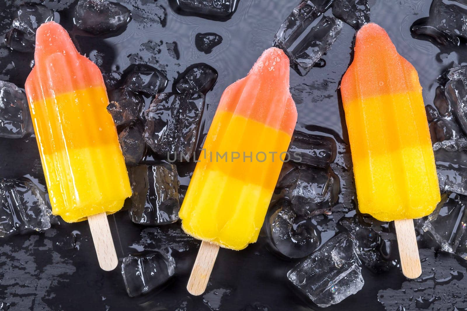 Fruit ice cream on stick over ice on black slate board. Focus on Popsicles.