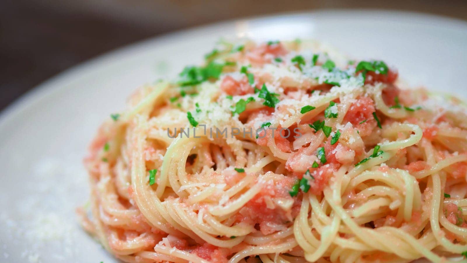 Close-up image of spaghetti sauce tarako which made from fresh cod fish in Japan and mixed with Thai coriander on the top of white plate and very famous italian-japanese menu dish in Thailand restaurant.