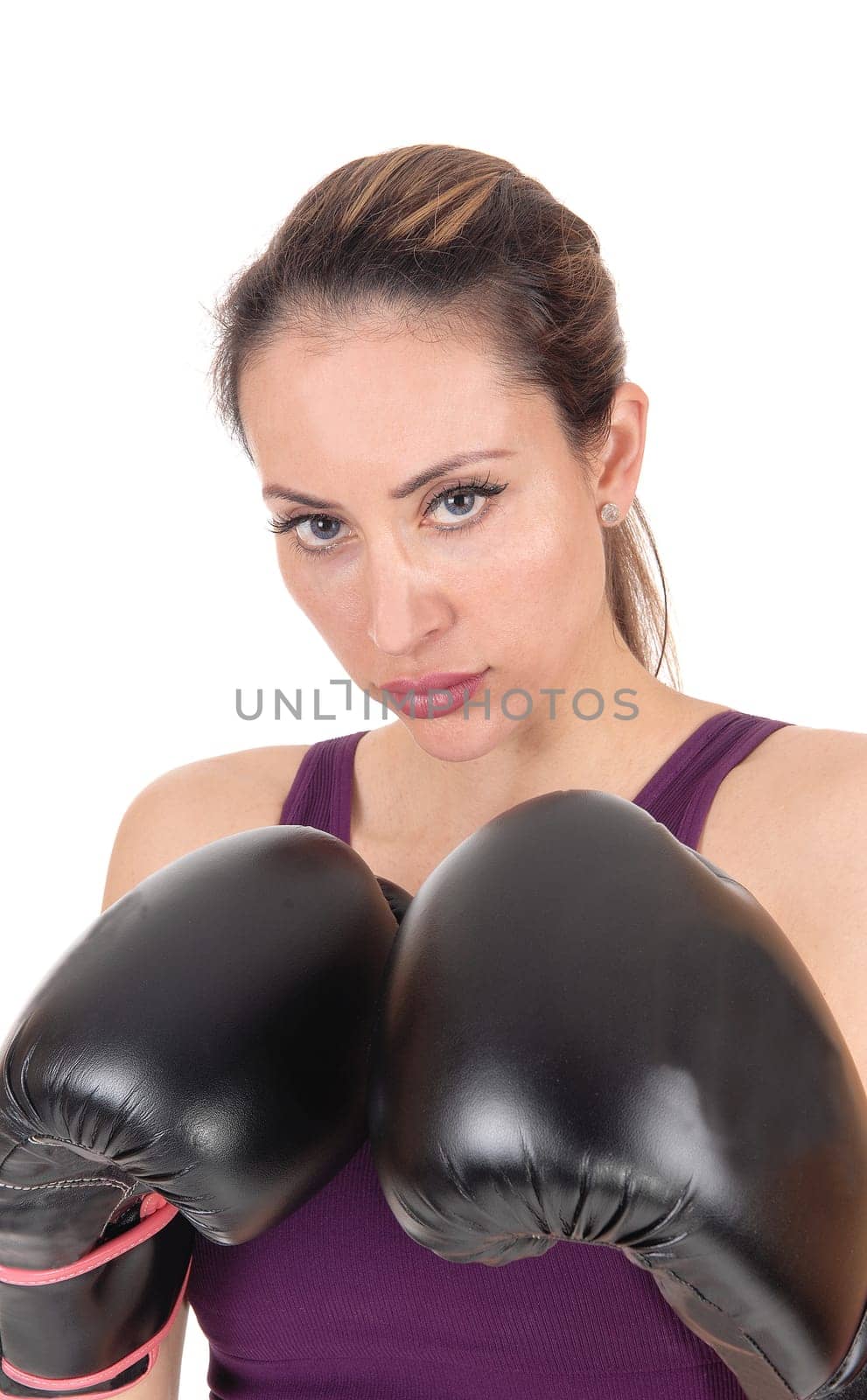 A serious looking young woman whit her black boxing gloves holding.up, looking into the camera, isolated for white background.