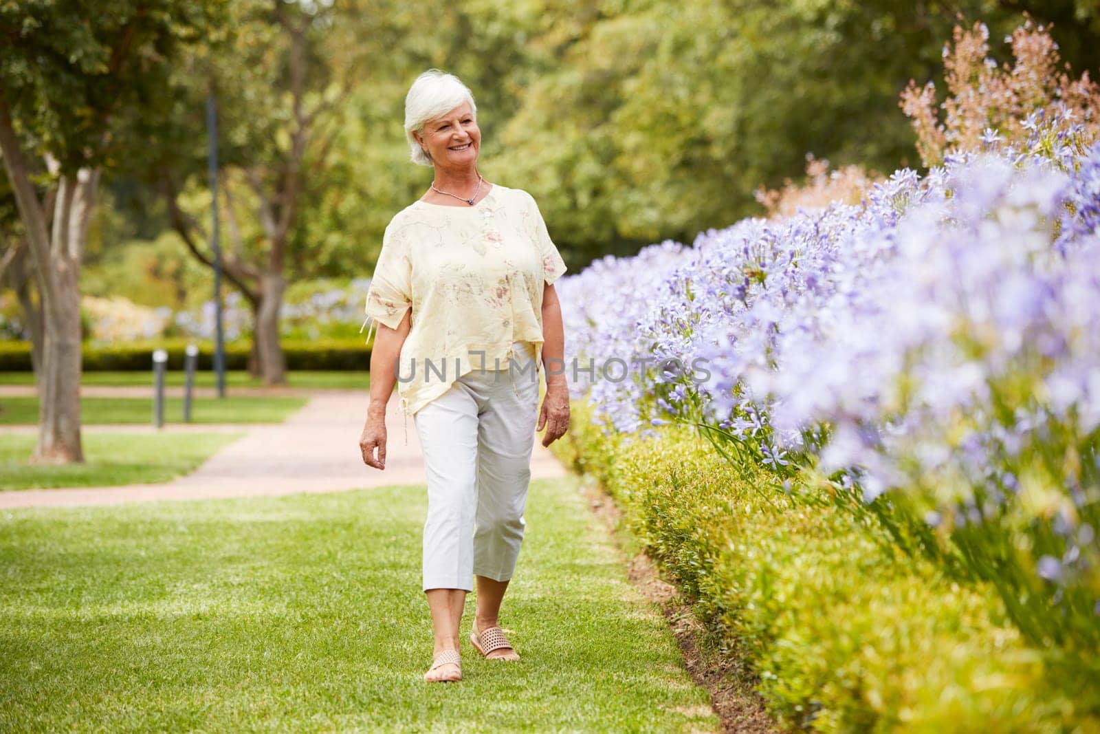 Senior Woman Enjoying Walk By Flower Beds In Park