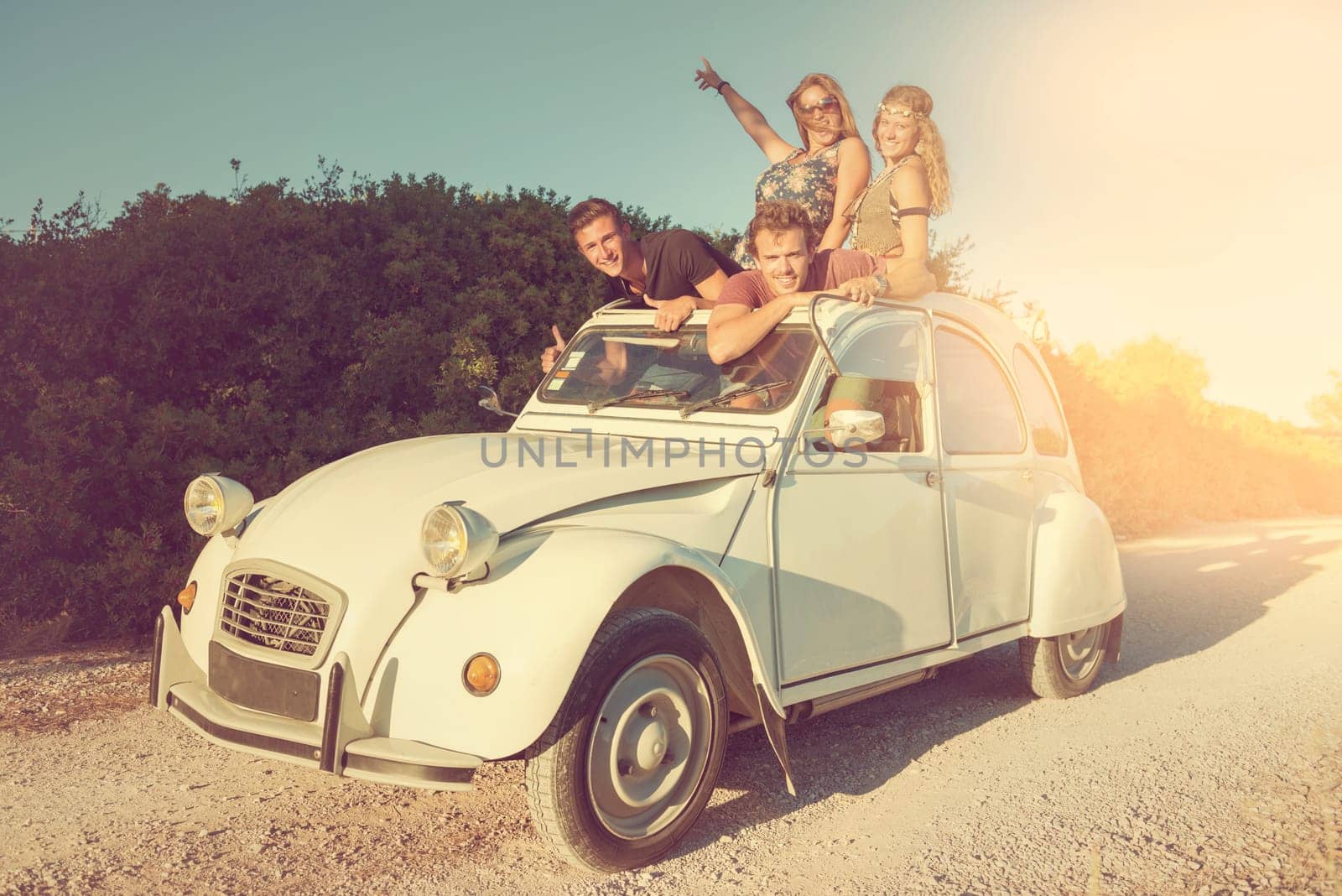 Group of happy friends in a car at sunset in summer.