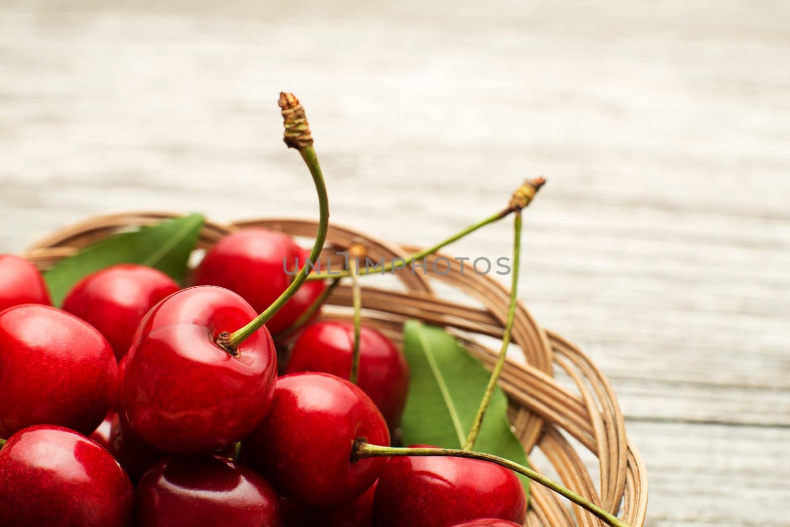Fresh red cherries in basket on wooden background close up
