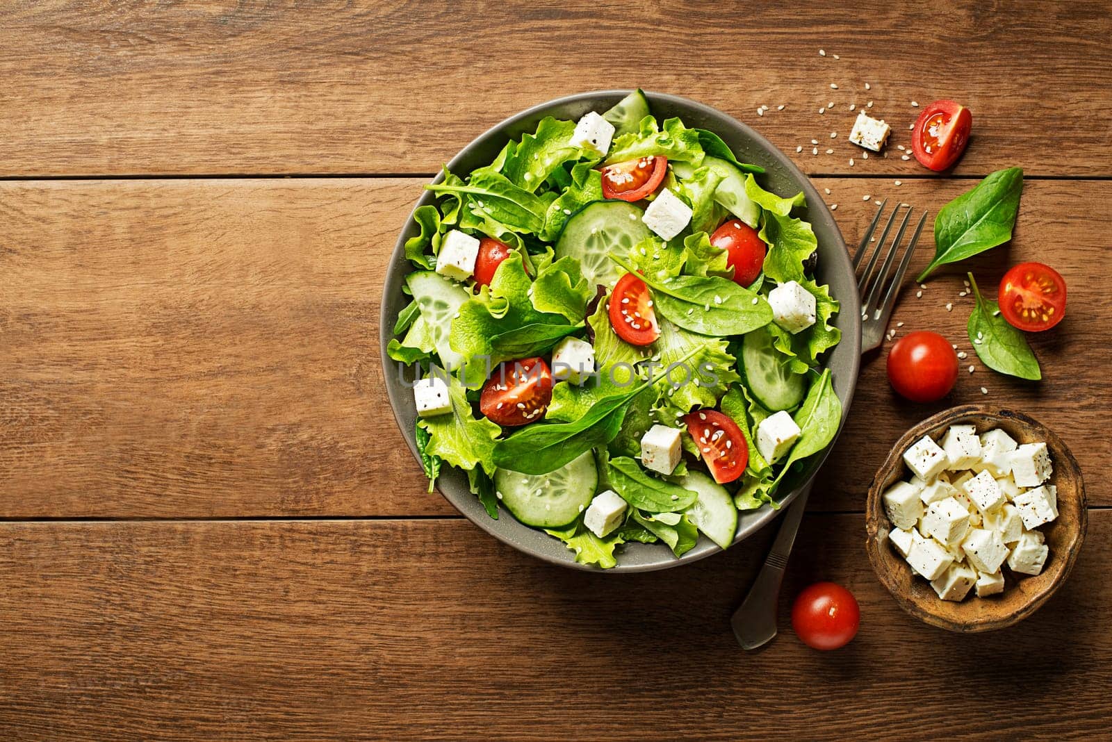 Green lettuce Salad with feta cheese and fresh vegetables on wooden background