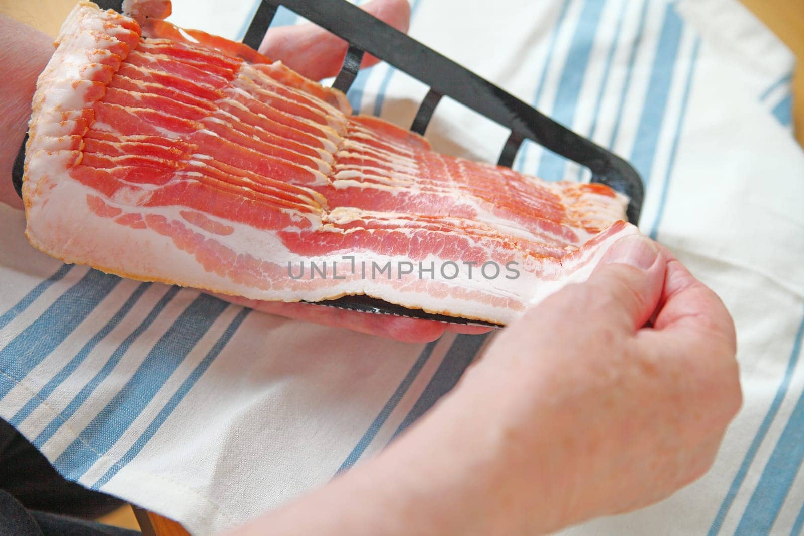 Older man pulls slice of raw bacon from package