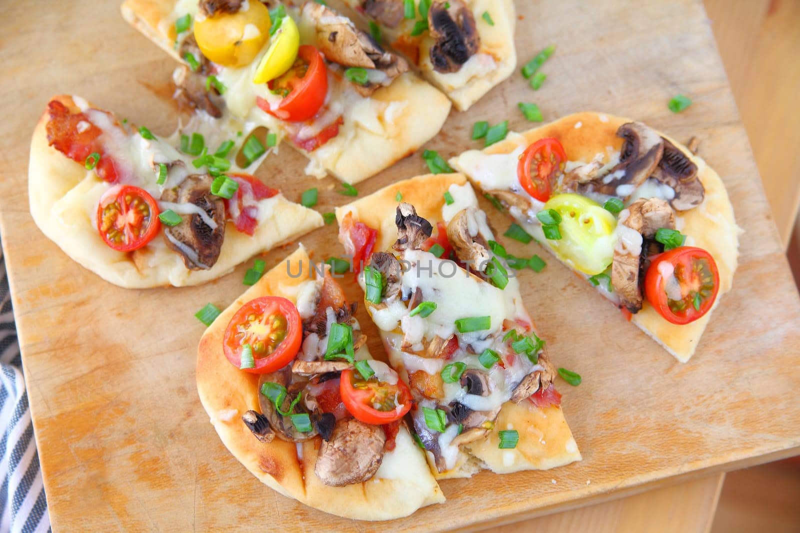 Naan pizzas with cherry tomatoes, mushrooms, bacon and scallions cut into portions