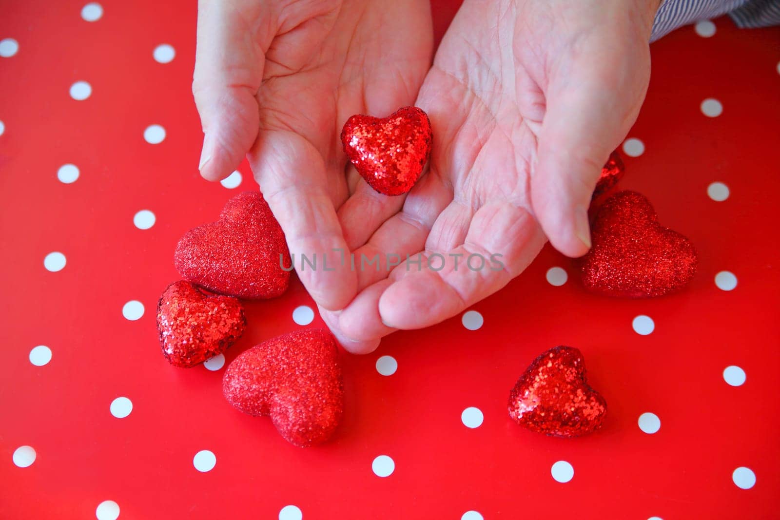Man with shiny heart in hands over more hearts on polka dot background