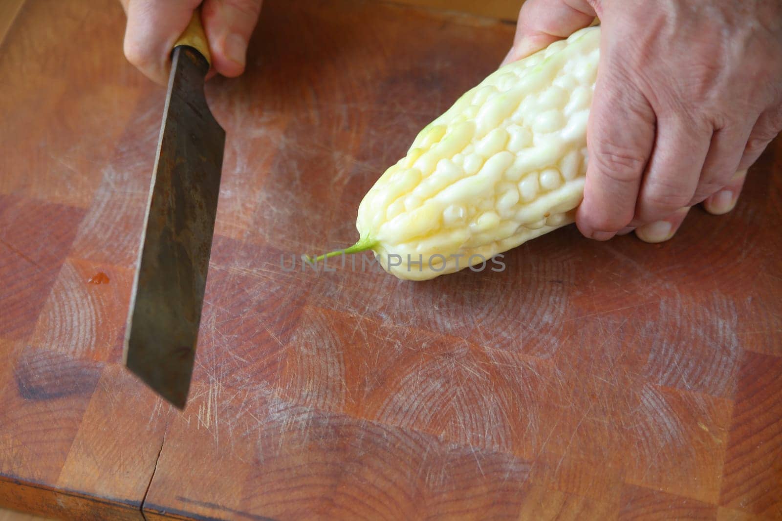 A male cook ready to cut up a Chinese bitter melon on a cutting board..