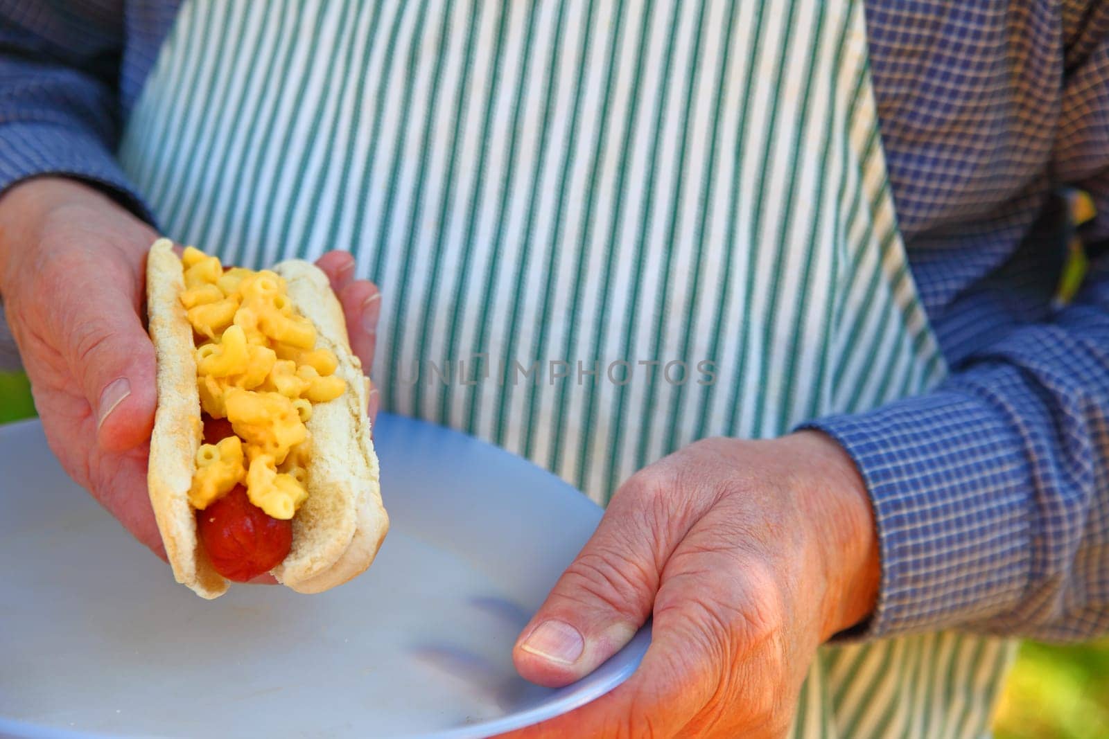 Man in apron with a hot dog topped with mac ’n cheese