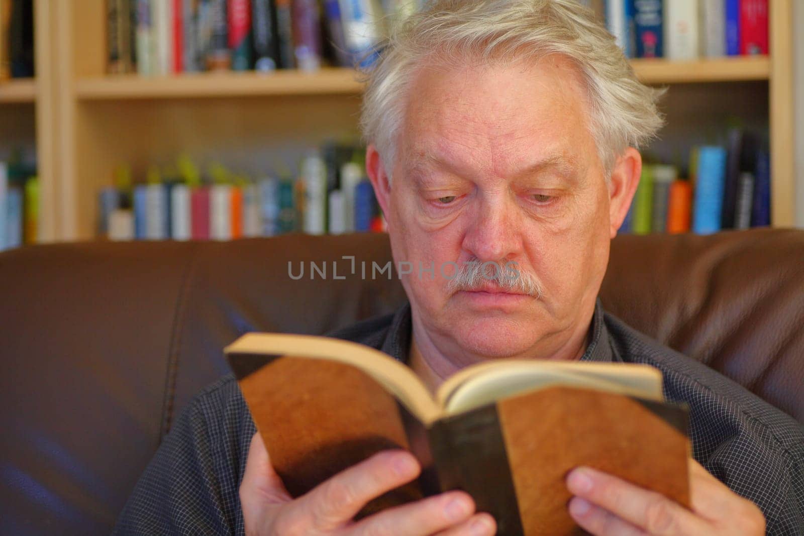 Mature man on a sofa in front of a bookcase with many books