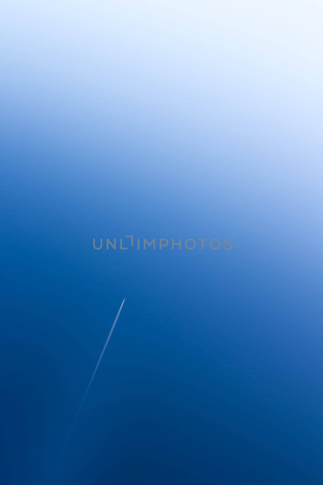 Airplane flying at high altitude leaving its white wake over blue sky