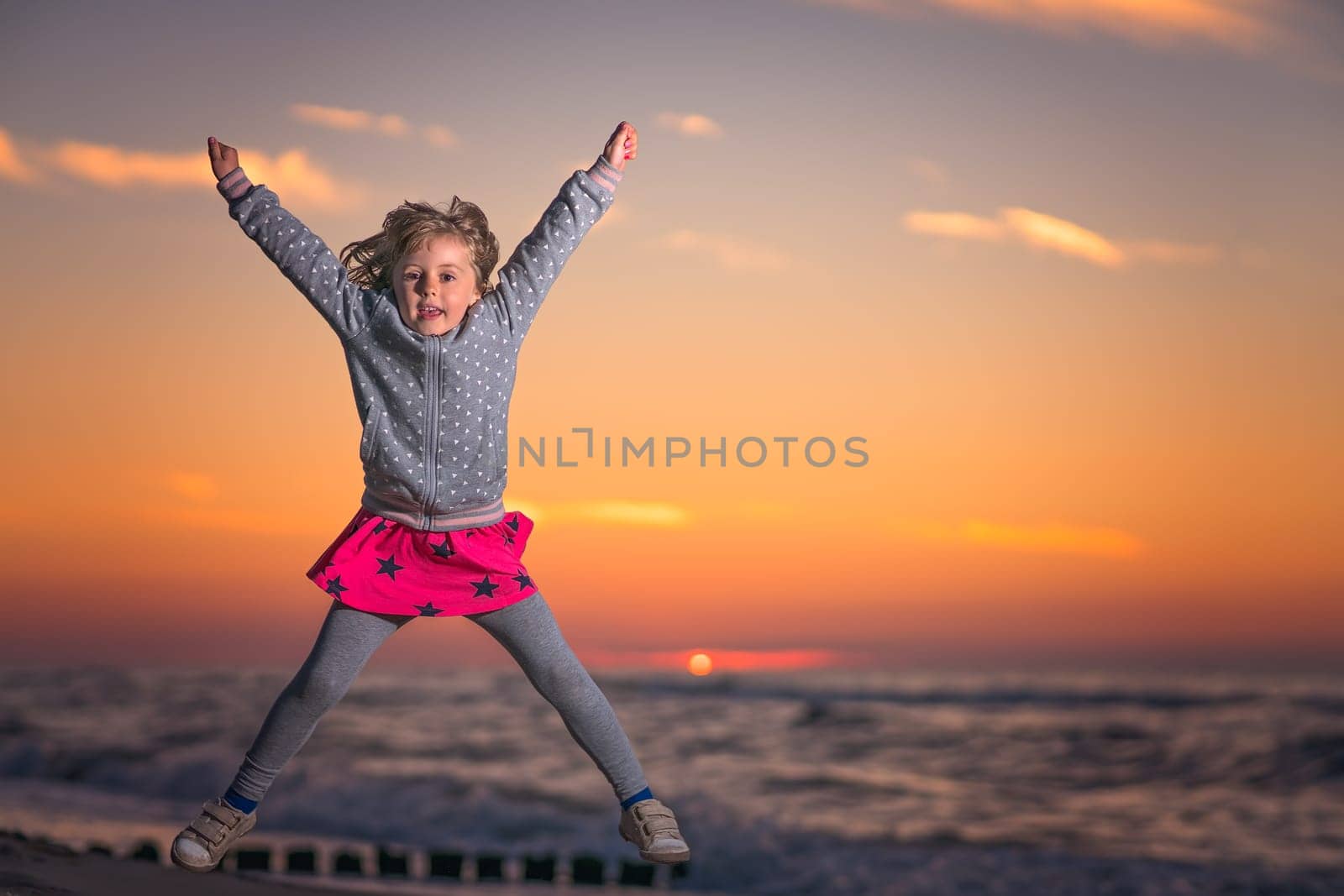 Cute little Caucasian girl jumping high on the beach at sunset in summer